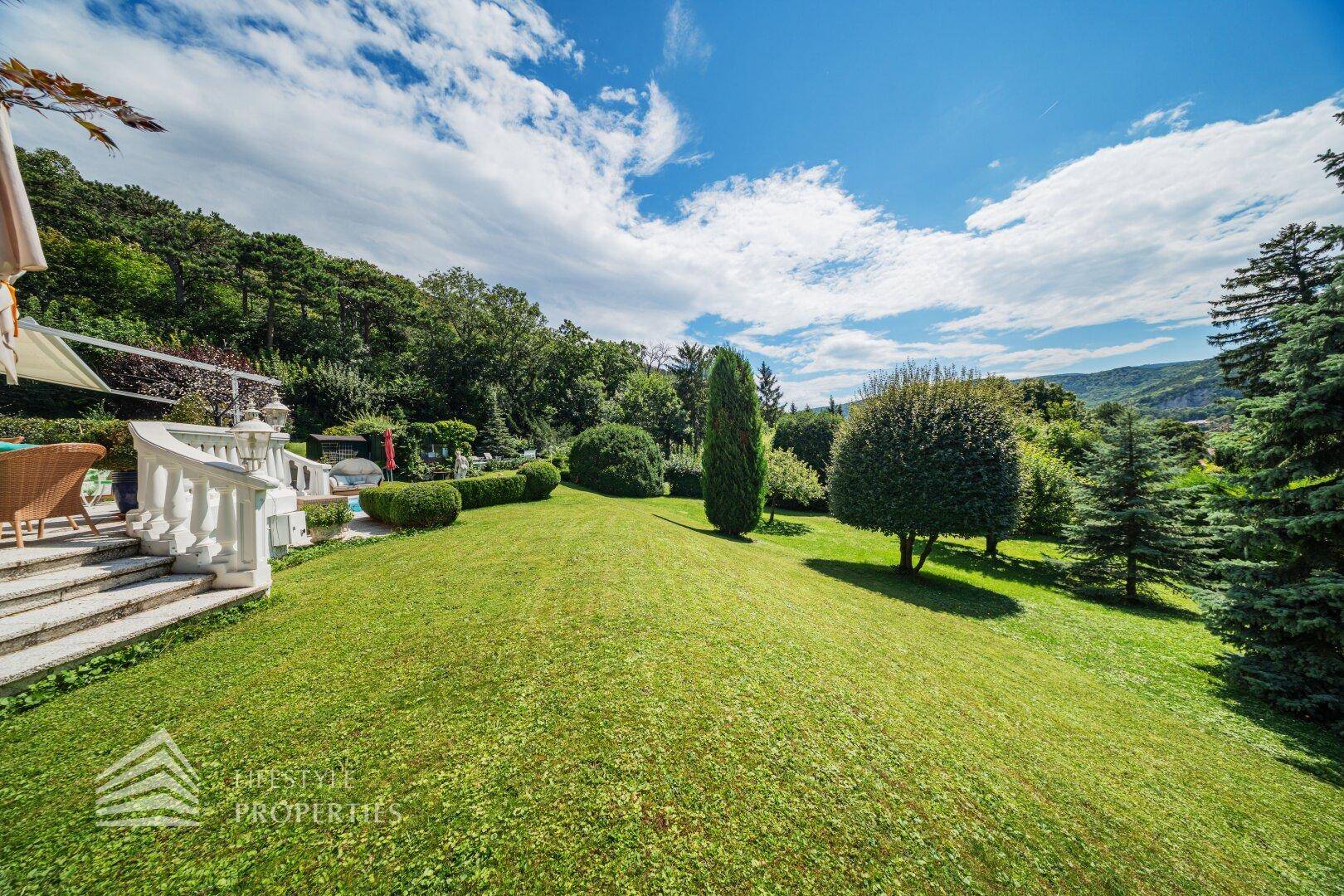 Weitläufiger, gepflegter Rasenbereich mit Blick auf die umliegenden Berge und die Terrasse der Villa.
