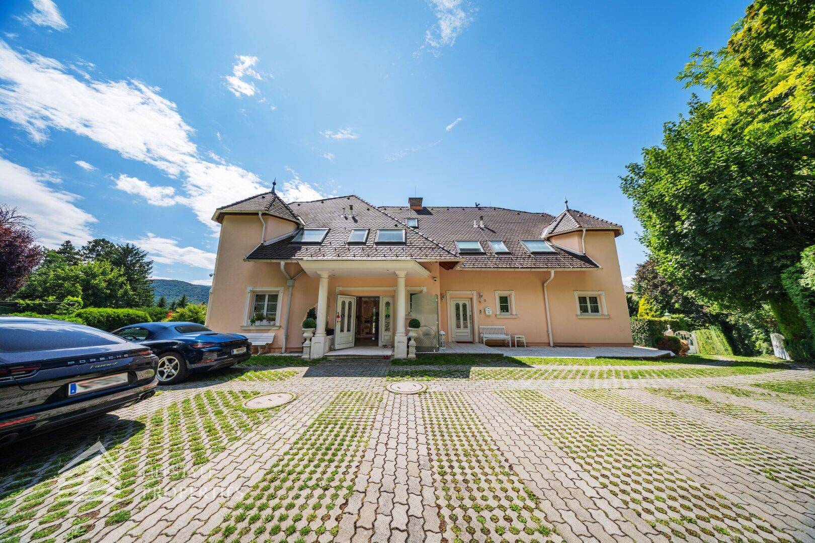 Die elegante Fassade der Villa mit Säulenportal und großzügiger Auffahrt mit Parkplätzen.