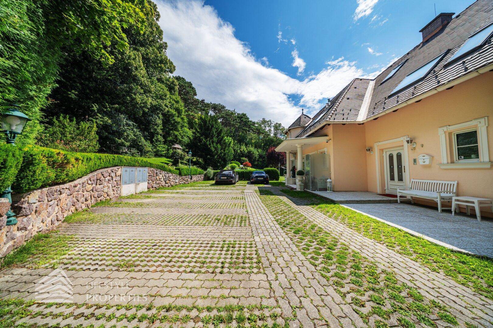 Die weitläufige Auffahrt der Villa mit Parkmöglichkeiten und gepflegter Steinmauer.