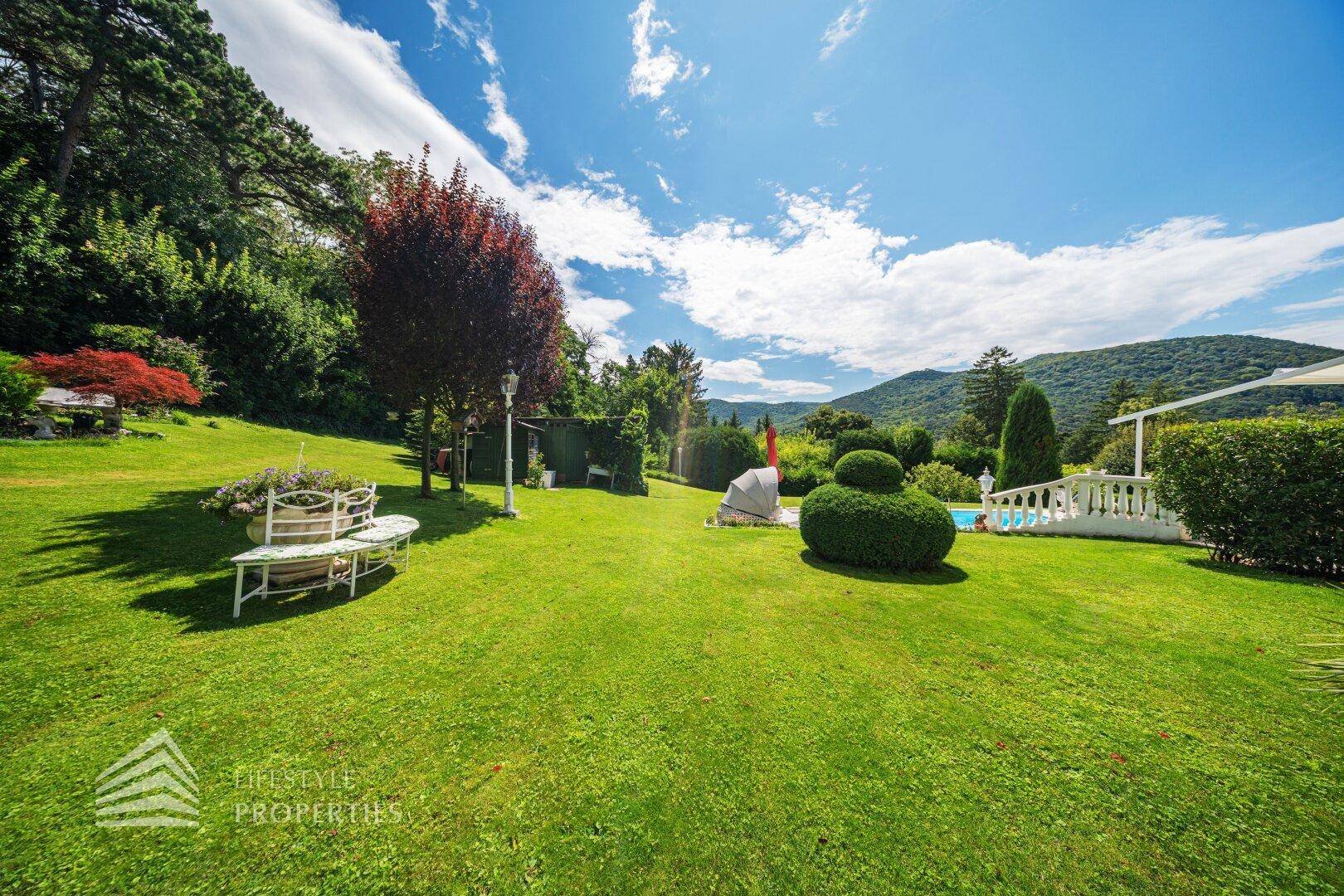 Der weitläufige Gartenbereich mit gepflegtem Rasen, Sitzgelegenheiten und Blick auf die Berge.