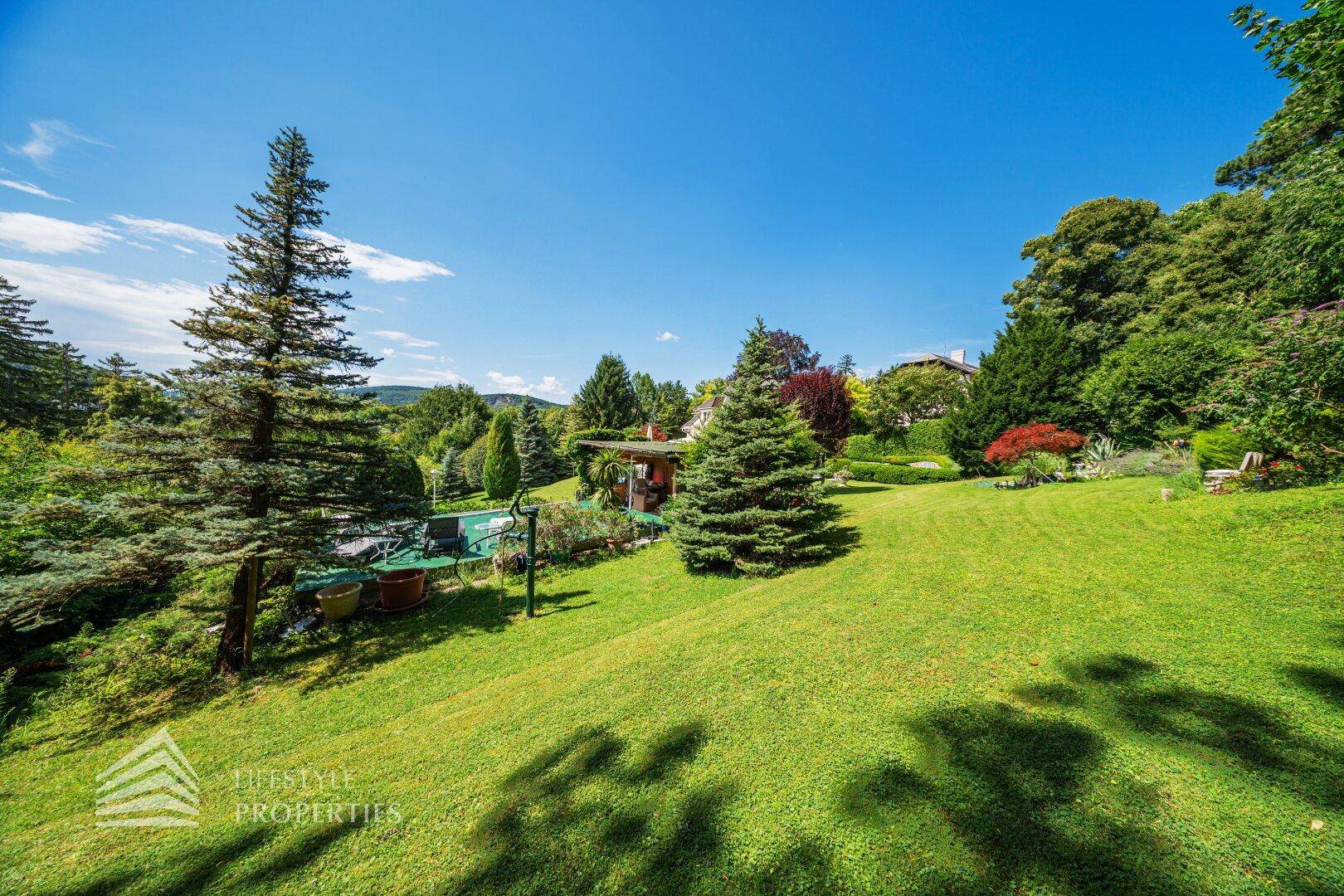 Der hügelige Gartenbereich mit hohen Nadelbäumen und weitem Blick in die Landschaft.