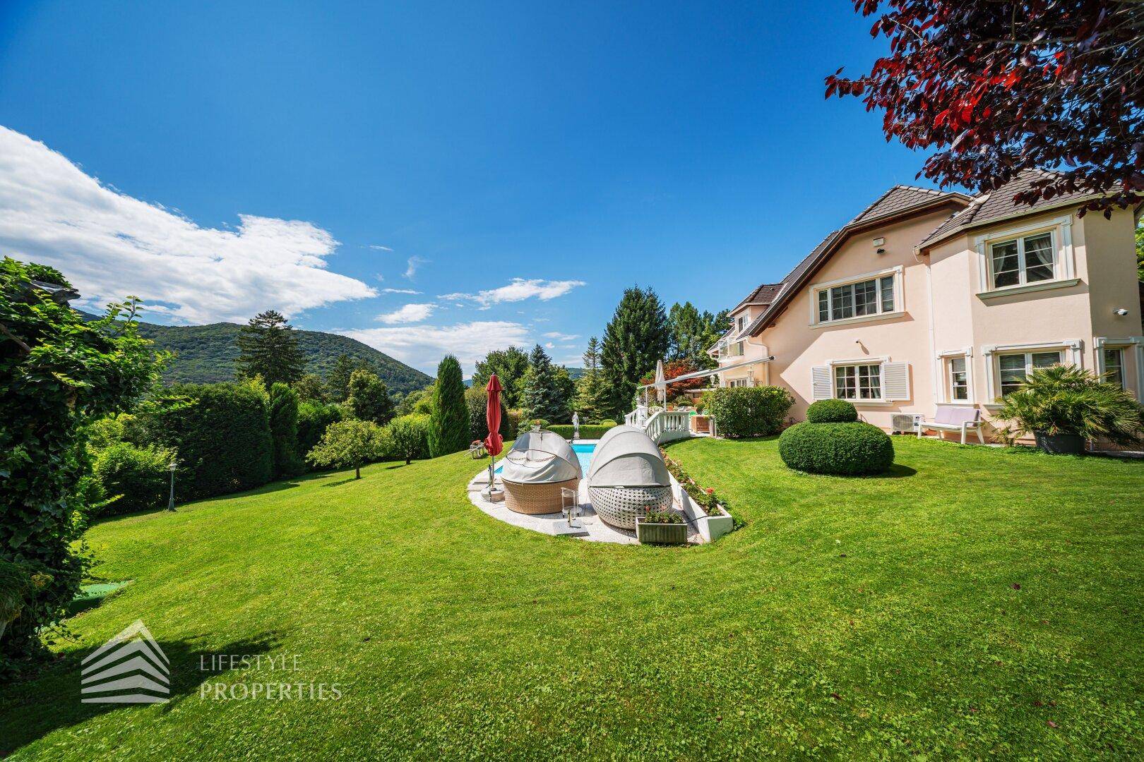 Der gepflegte Garten mit Liegeflächen, Pool und der eleganten Villa im Hintergrund.