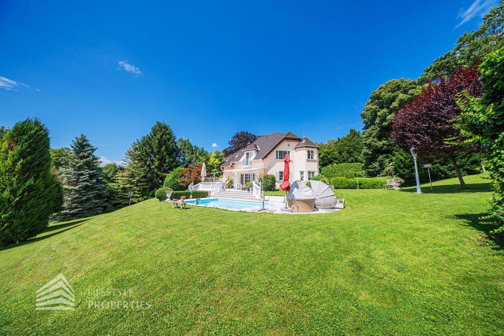 Die luxuriöse Villa mit großem Pool und weitläufigem, gepflegtem Garten unter blauem Himmel.