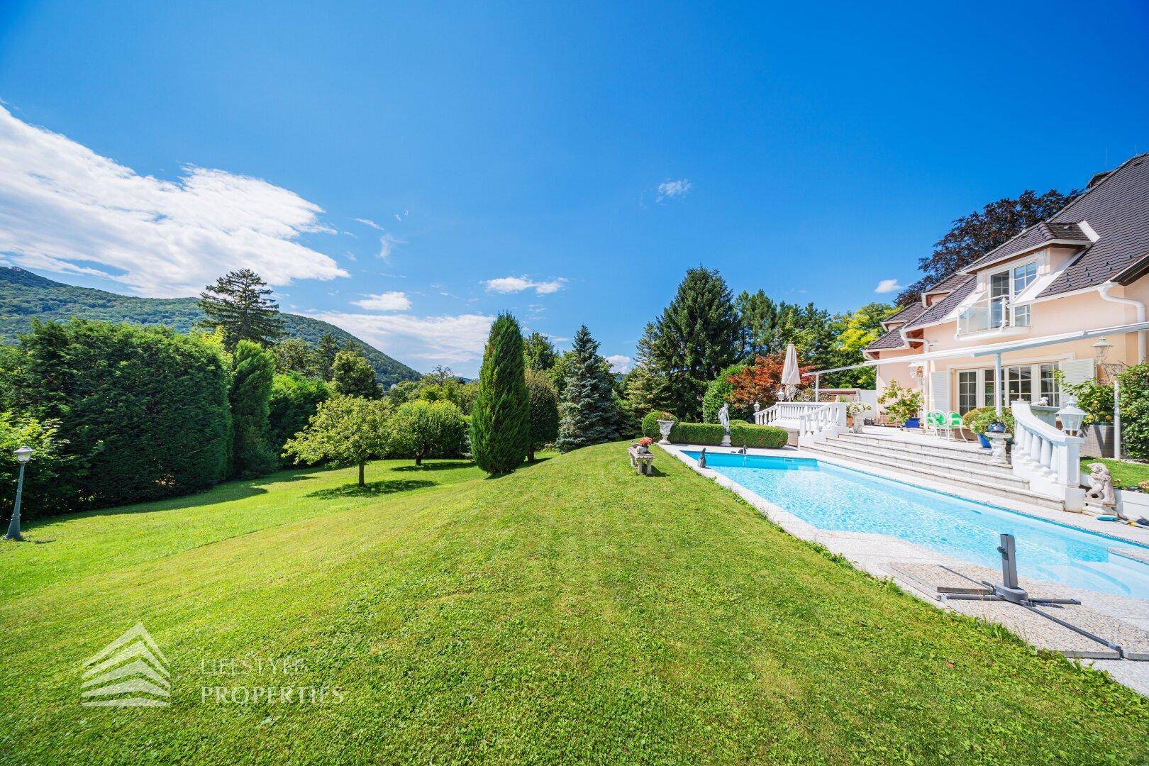 Der weitläufige Garten mit Pool und Terrasse, umgeben von grünen Hügeln und Bäumen.