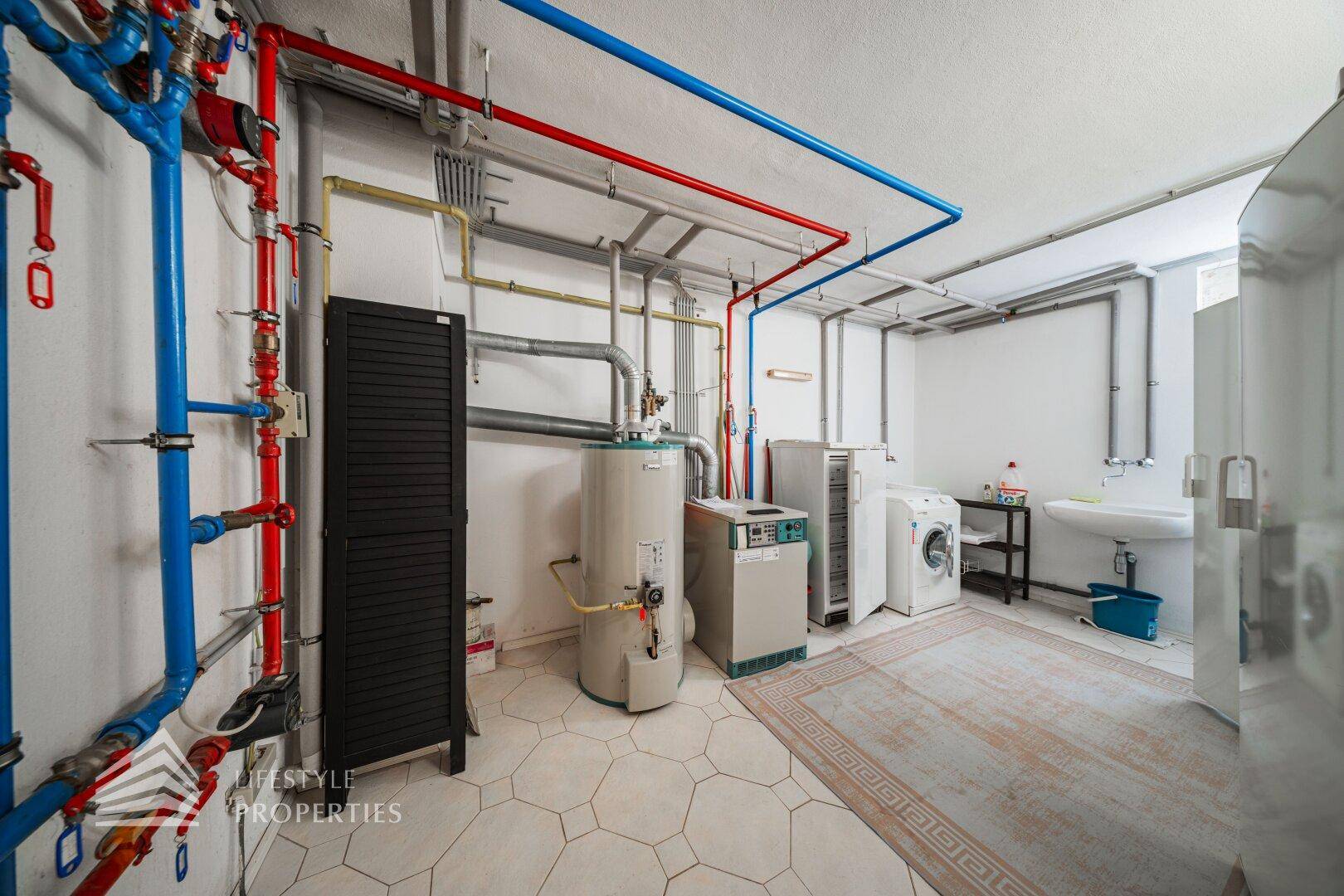 Technikraum mit Heizungsanlage, Warmwasserboiler und Waschbereich.