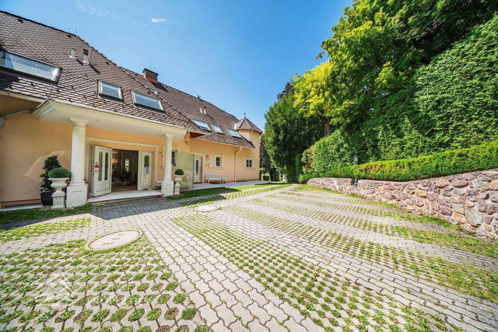 Die repräsentative Einfahrt zur Villa mit Säulenportal und umgebender grüner Hecke.