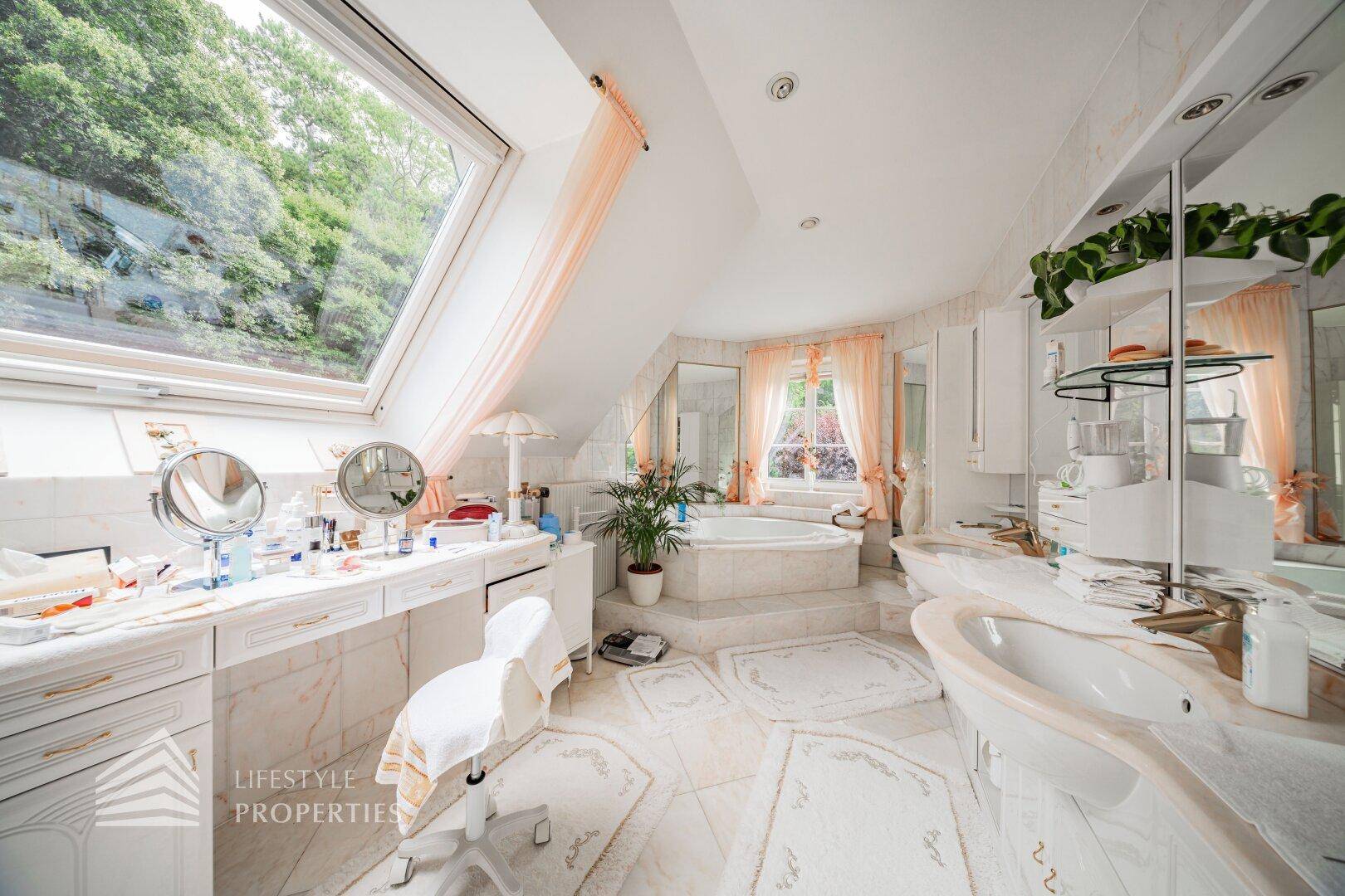 Großzügiges Badezimmer mit Whirlpool, Doppelwaschbecken und großer Dachfensterfront.