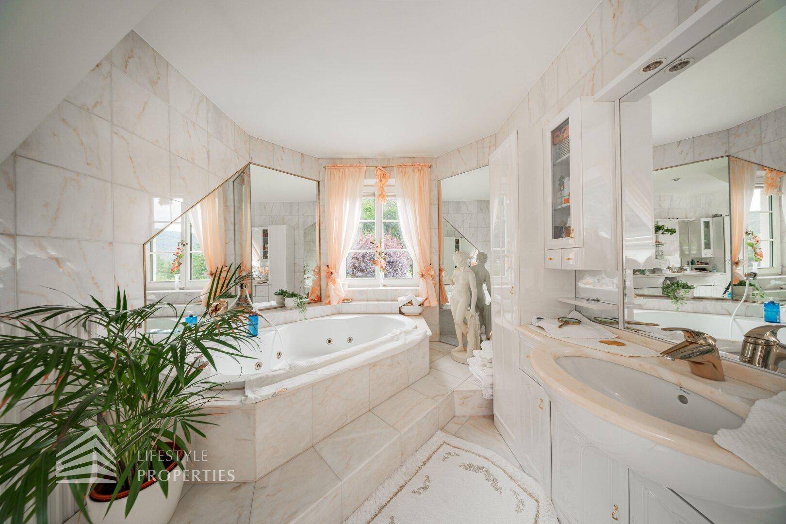 Elegantes Badezimmer mit Whirlpool, Marmorfliesen und Fenster mit Blick ins Grüne.