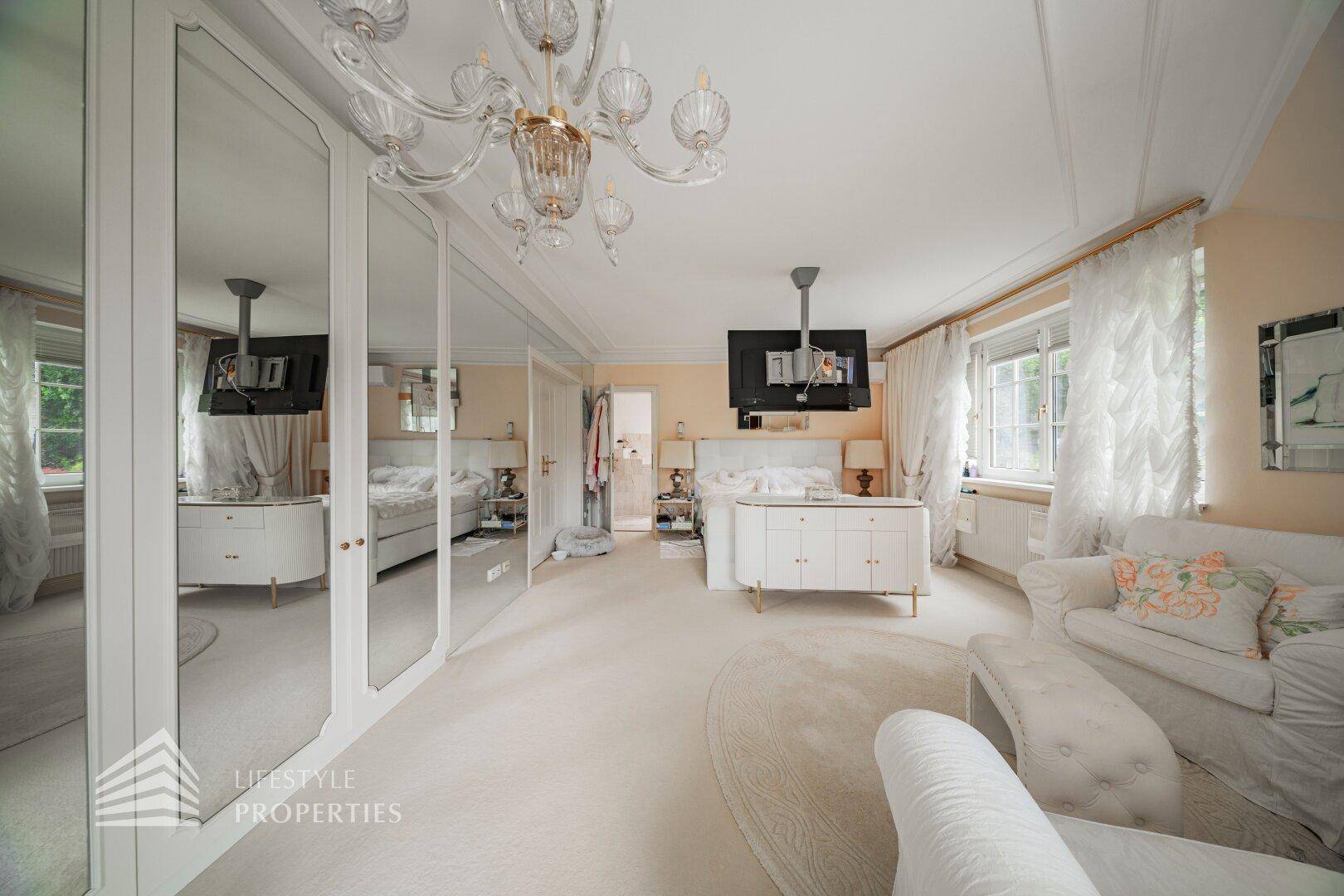 Helles Schlafzimmer mit großem Bett, Spiegelschränken und einem eleganten Kronleuchter.