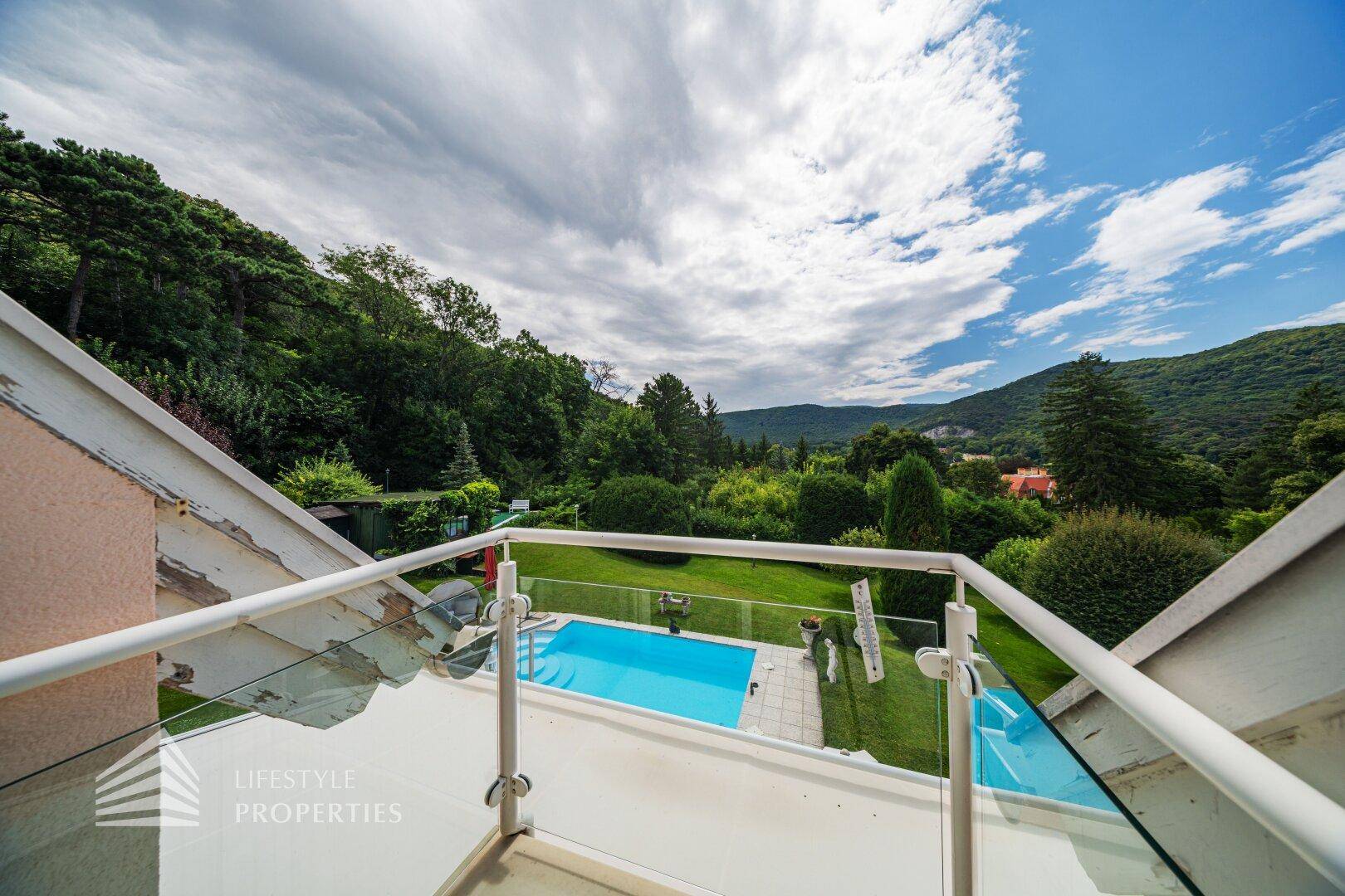 Balkon mit Glasgeländer bietet einen weiten Blick auf den Pool und die umliegende grüne Landschaft.