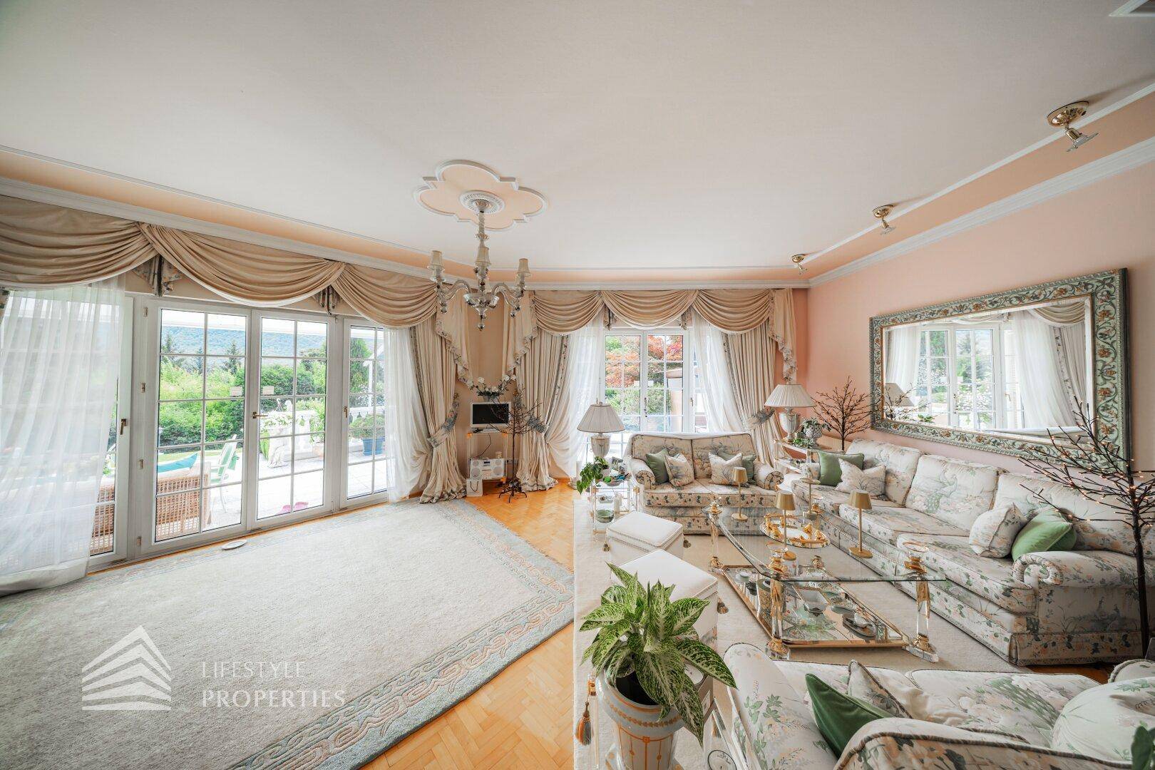 Geräumiges Wohnzimmer mit großen Fenstertüren, die zum Außenbereich führen, und klassischer Einrichtung.