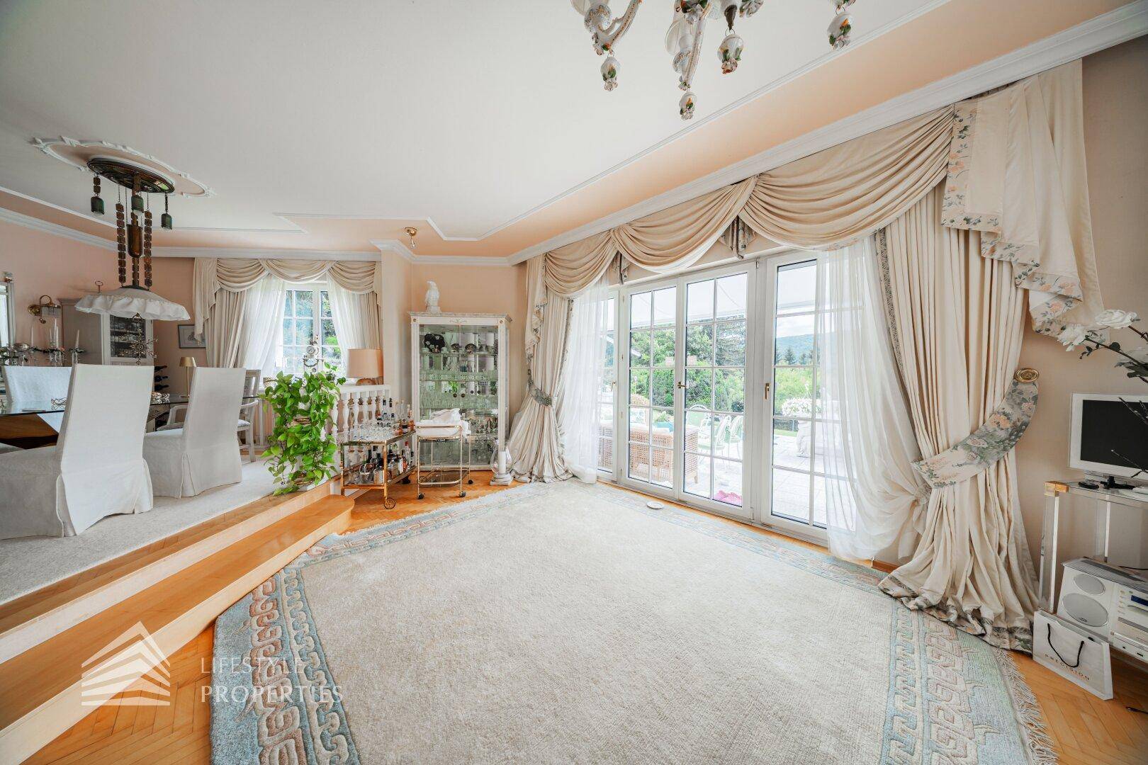 Heller Wohnbereich mit großen Fenstertüren, die Zugang zum Außenbereich bieten, und eleganten Vorhängen.