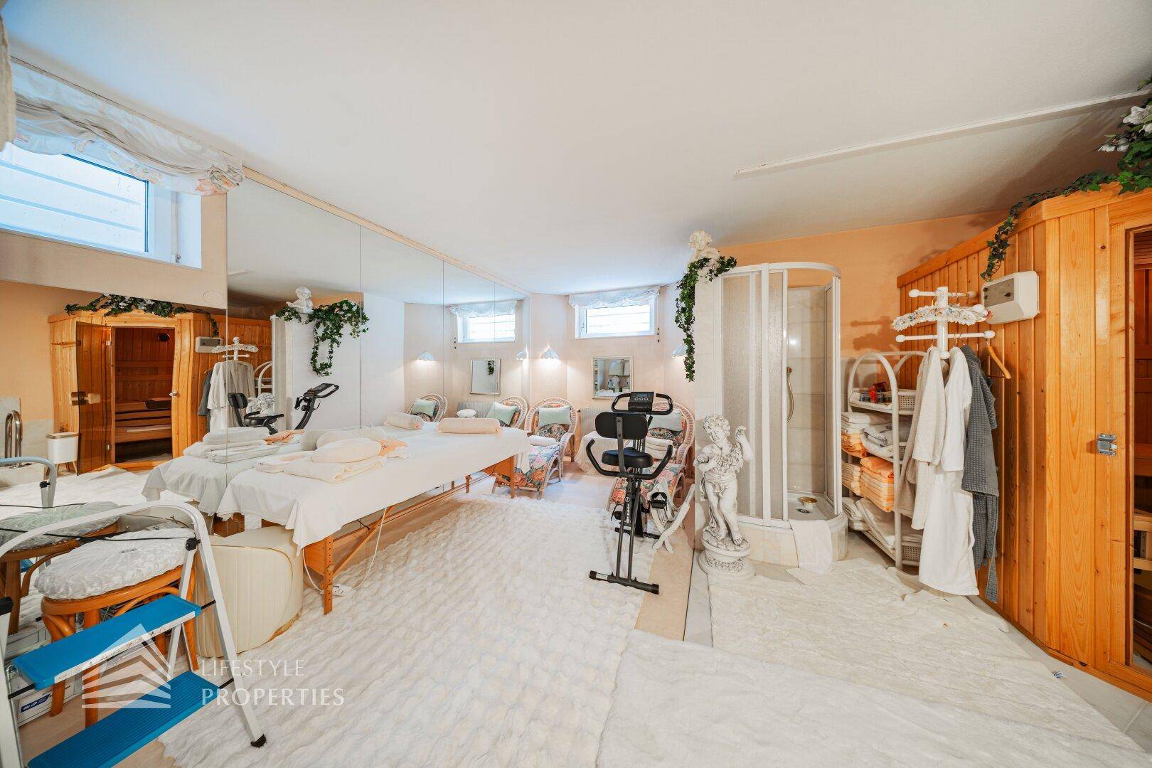 Großer Wellness- und Fitnessbereich mit Massageliege, Trainingsgeräten, Sauna und Dusche.