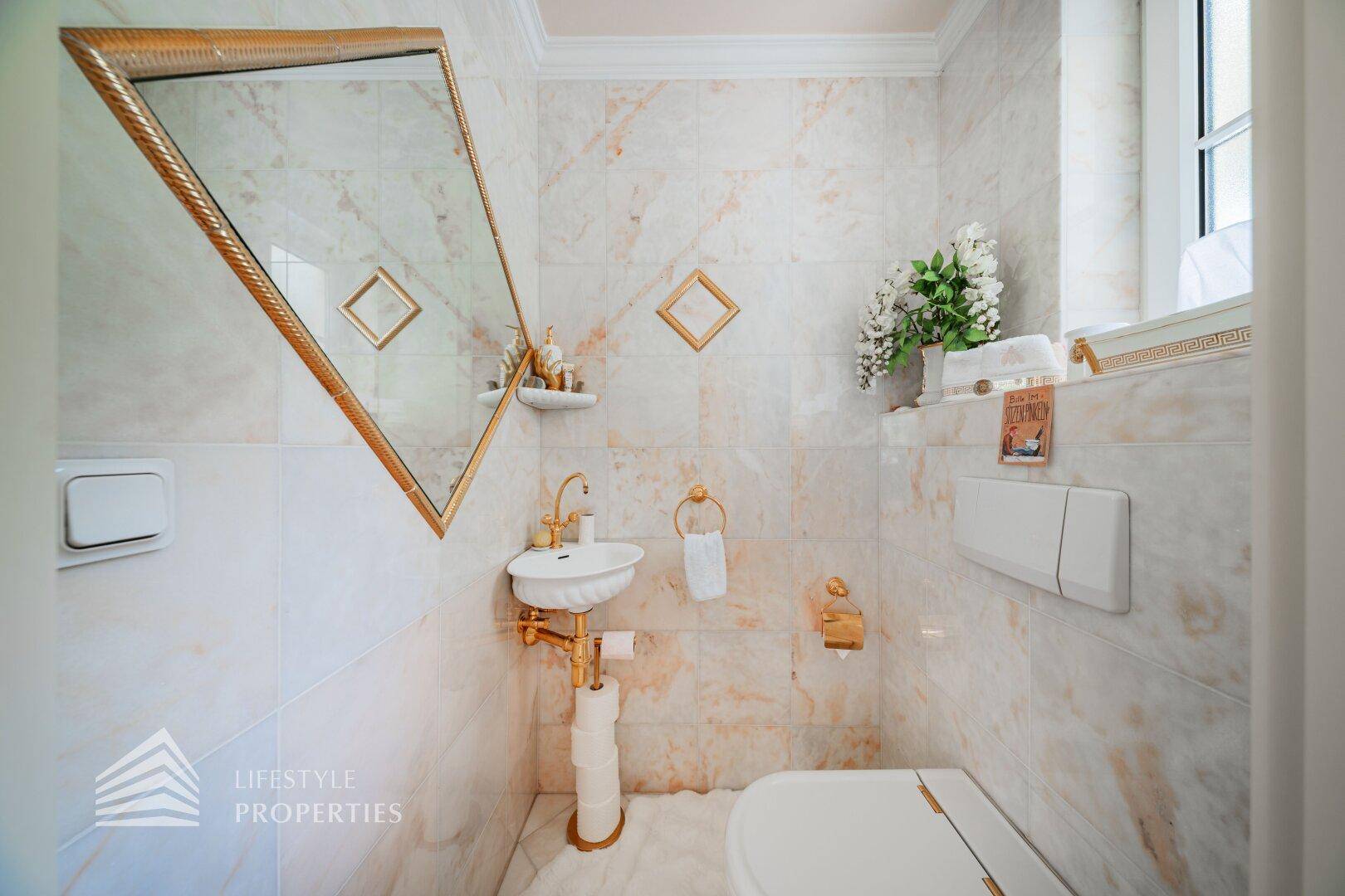 Elegantes Gäste-WC mit Marmorfliesen, goldenen Armaturen und kleinem Waschbecken.
