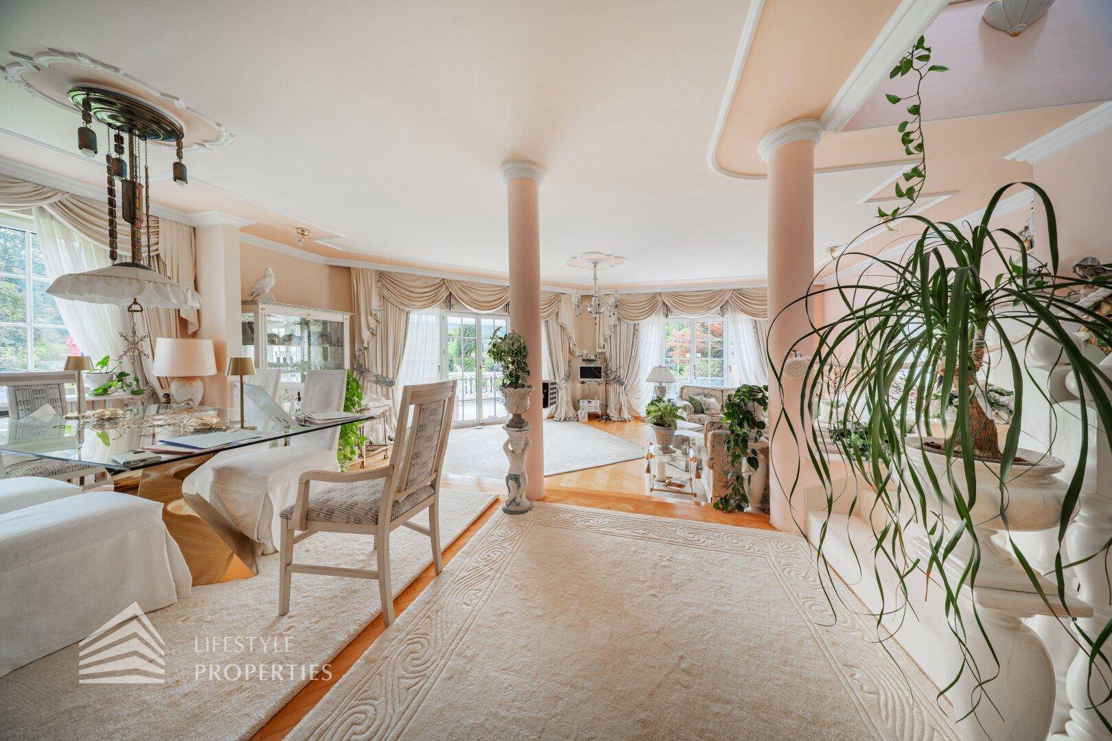 Weitläufiger Wohn- und Essbereich mit Säulen, vielen Pflanzen und elegantem Interieur.