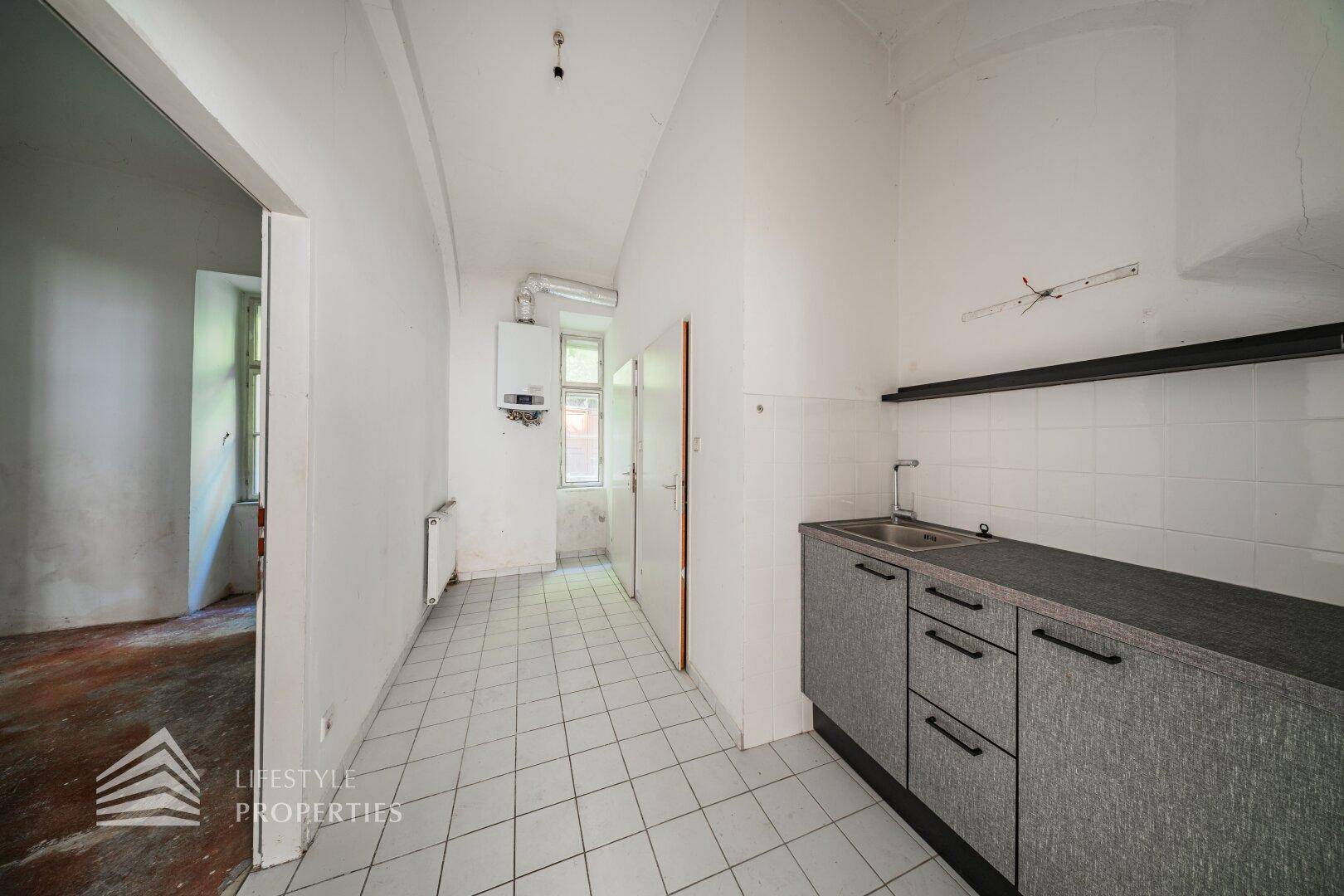 Einfache Küche mit Fliesenboden, Spüle und Gastherme, bereit für eine Modernisierung.