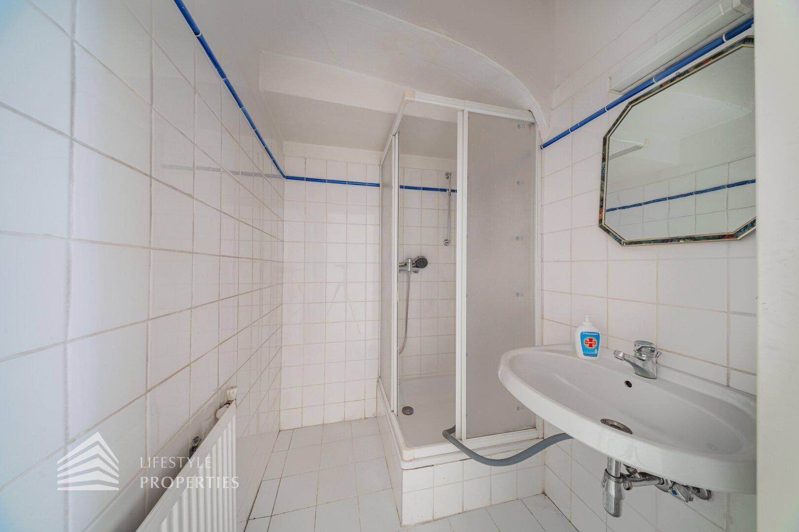 Badezimmer mit Duschkabine, Waschbecken und Fliesen, in einem einfachen, funktionalen Zustand.