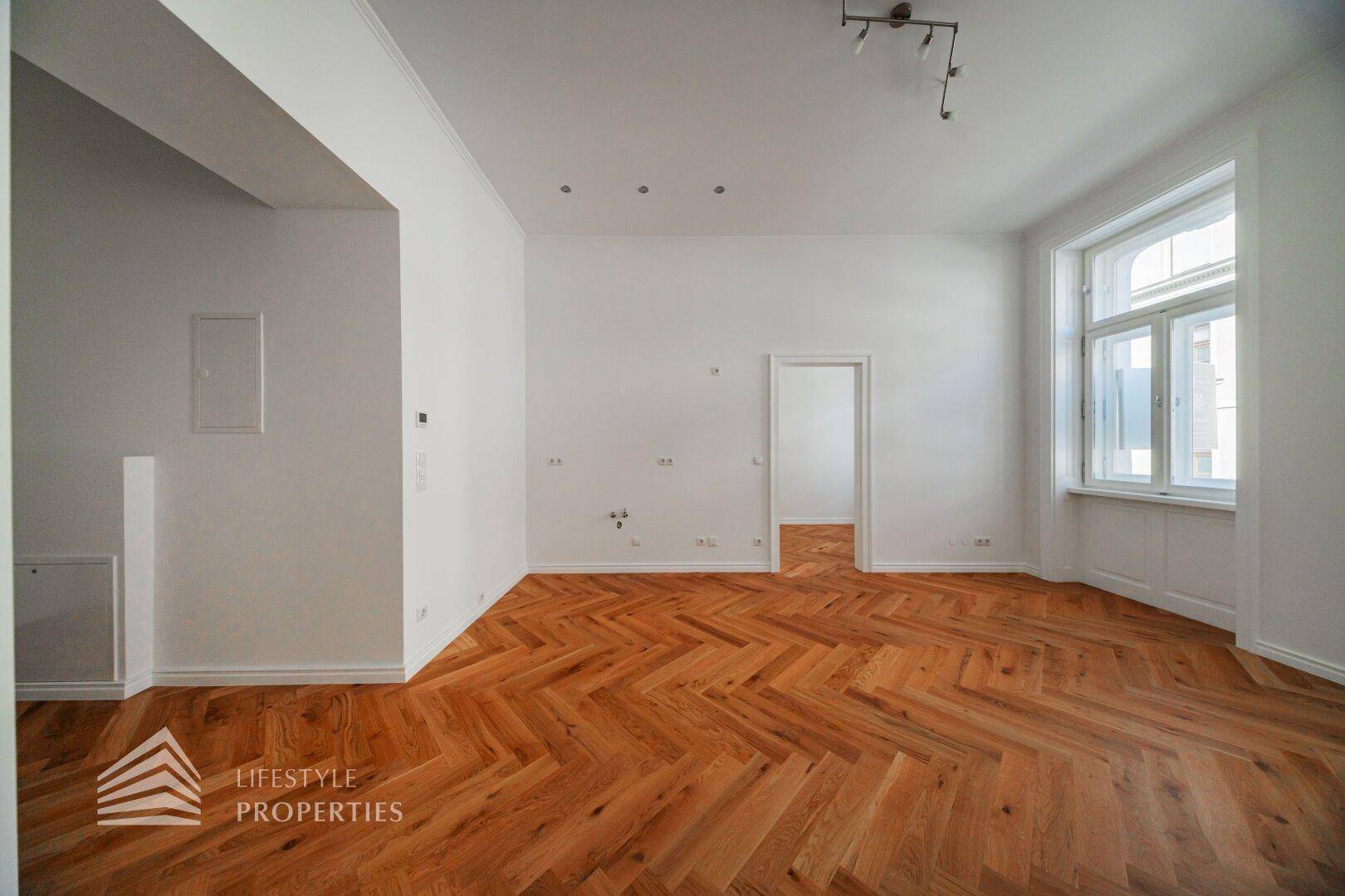 Geräumiges, helles Zimmer mit klassischem Fischgrätparkett und hohen Fenstern.
