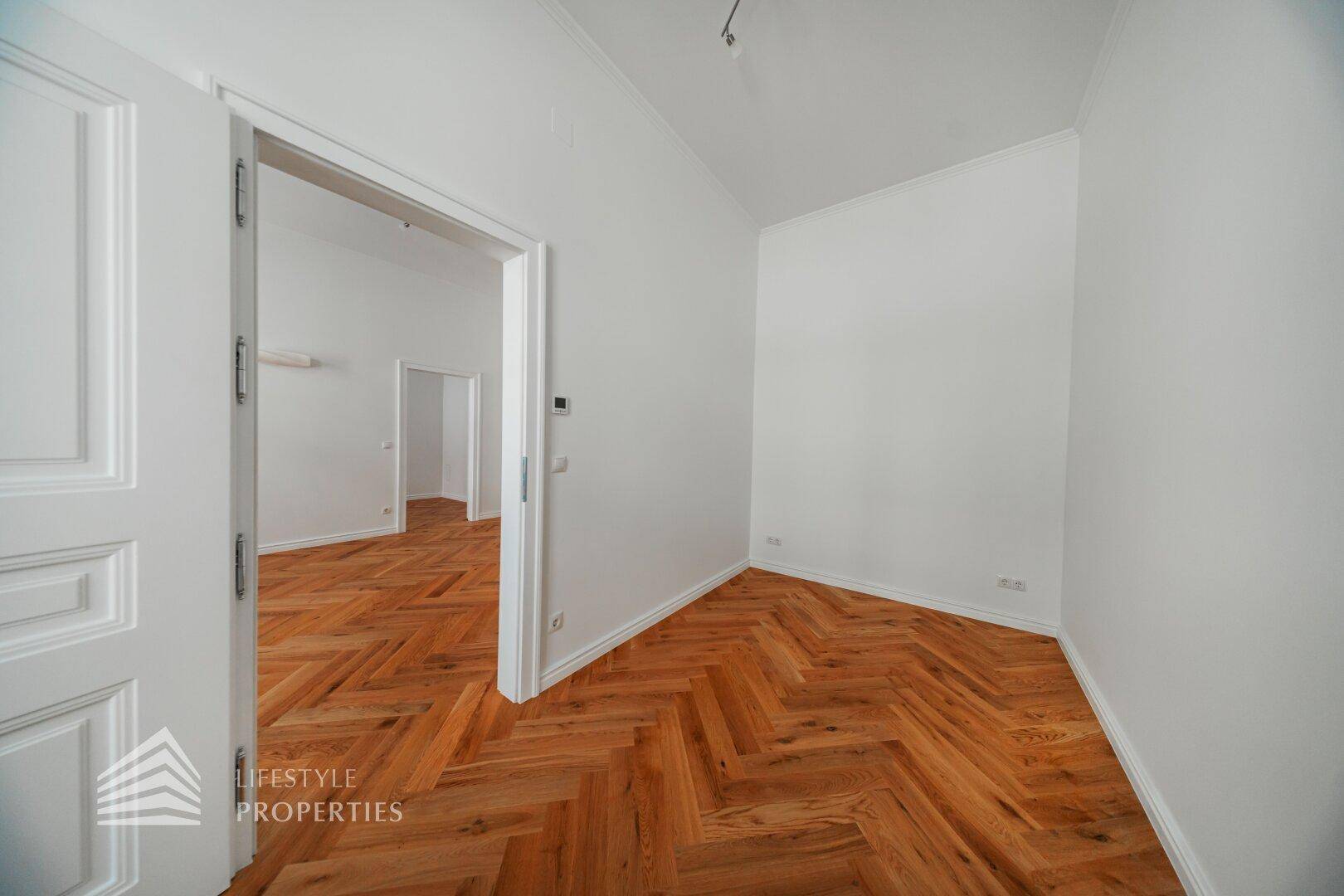 Leeres Zimmer mit Fischgrätparkett und hohen Türen, das viel Gestaltungspotenzial bietet.