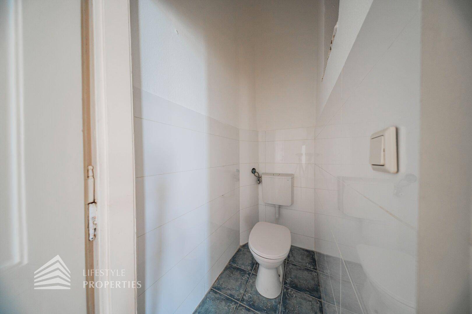 Kleines separates WC mit Fliesenboden und Wand-WC, funktional und einfach gehalten.