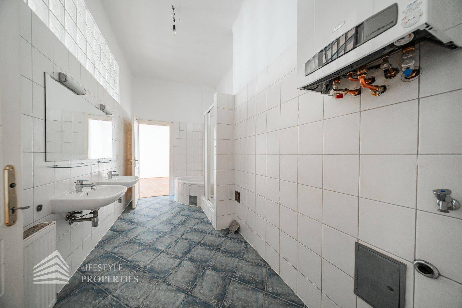 Langes Badezimmer mit zwei Waschbecken, Badewanne und Duschkabine, gefliest in Weiß und Blau.