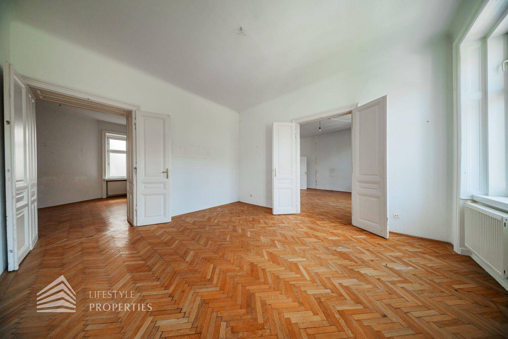 Großes, helles Zimmer mit Fischgrätparkett und mehreren Türen, das vielseitig nutzbar ist.
