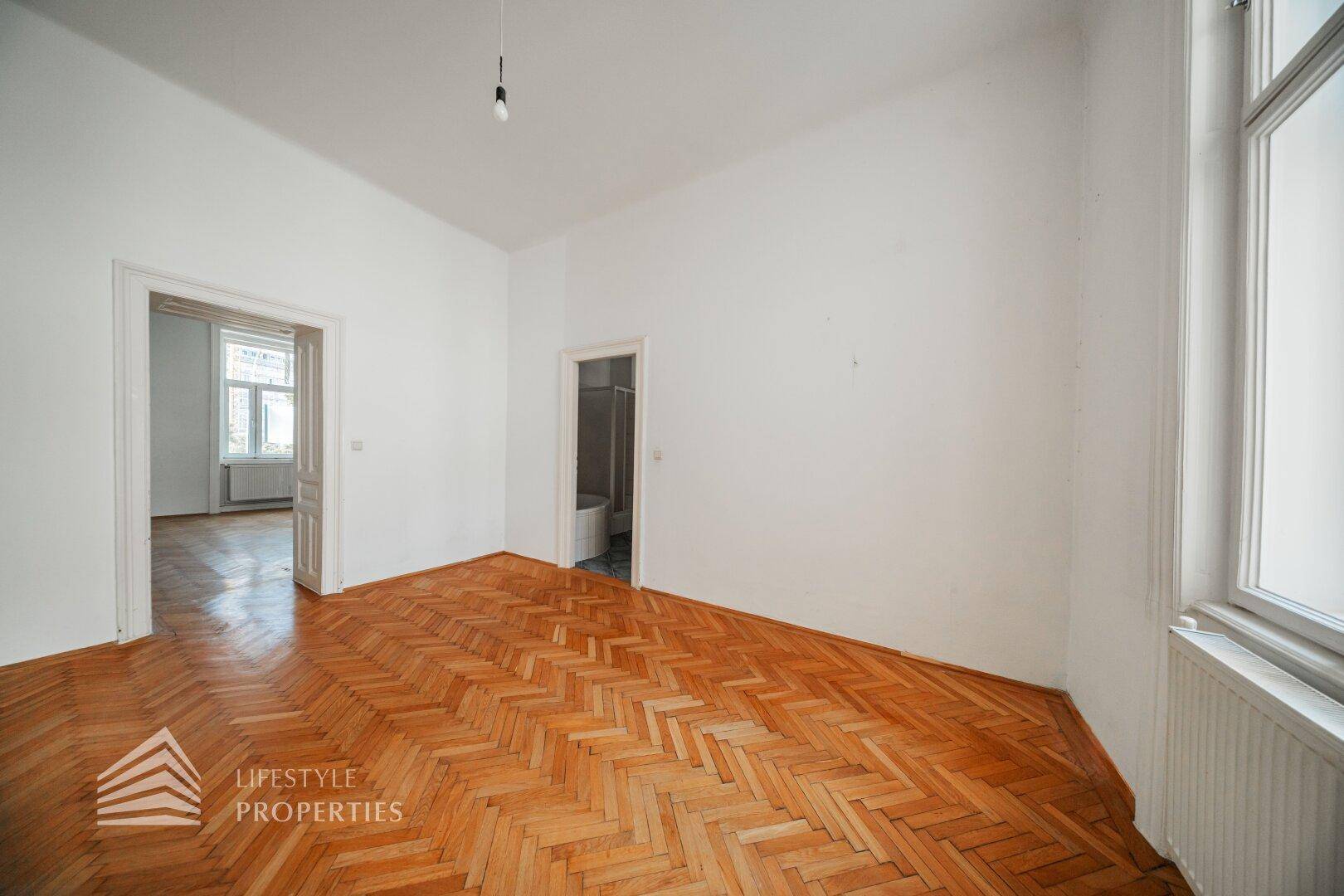 Geräumiges Zimmer mit Fischgrätparkett und Zugang zu weiteren Räumen, ideal für eine Familie.