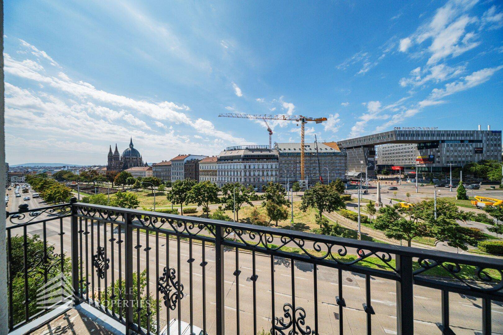 Sonniger Balkon mit Blick auf die Stadt, historische Gebäude und den blauen Himmel.