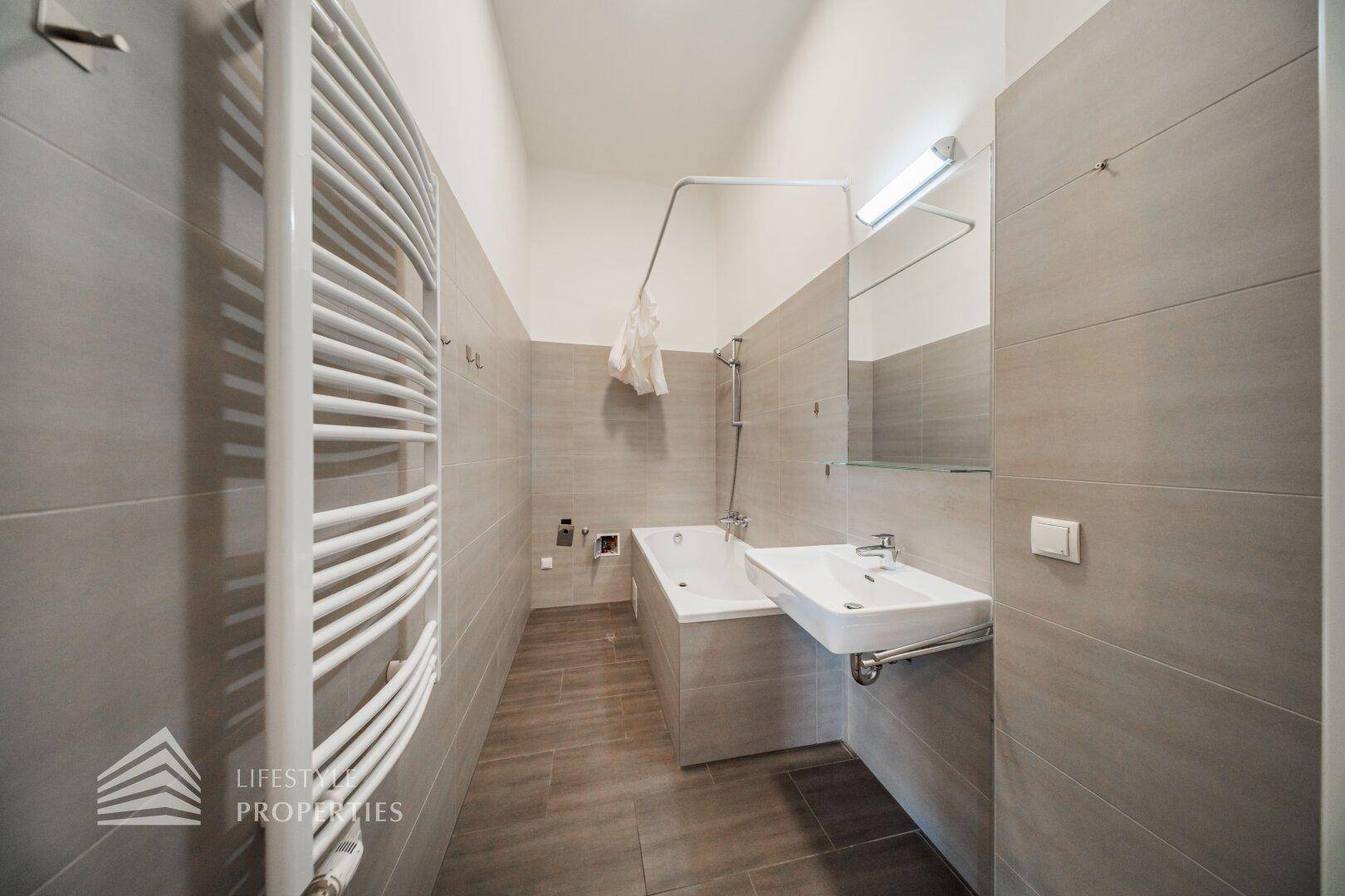 Modernes Badezimmer mit Badewanne, Waschbecken und beheiztem Handtuchhalter in neutralen Farbtönen.