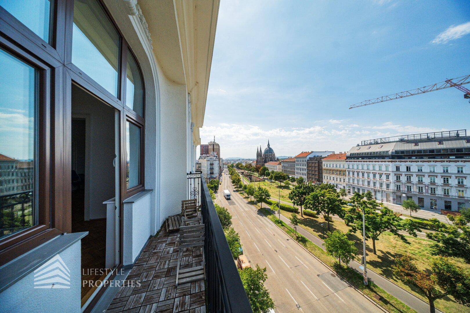 Balkon mit Holzboden und weitem Blick über die belebte Stadtstraße unter blauem Himmel.