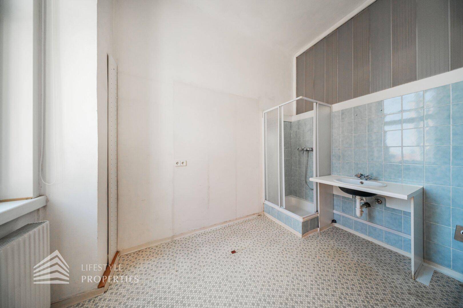 Badezimmer mit blauen Fliesen, Duschkabine und Waschbecken, renovierungsbedürftig.