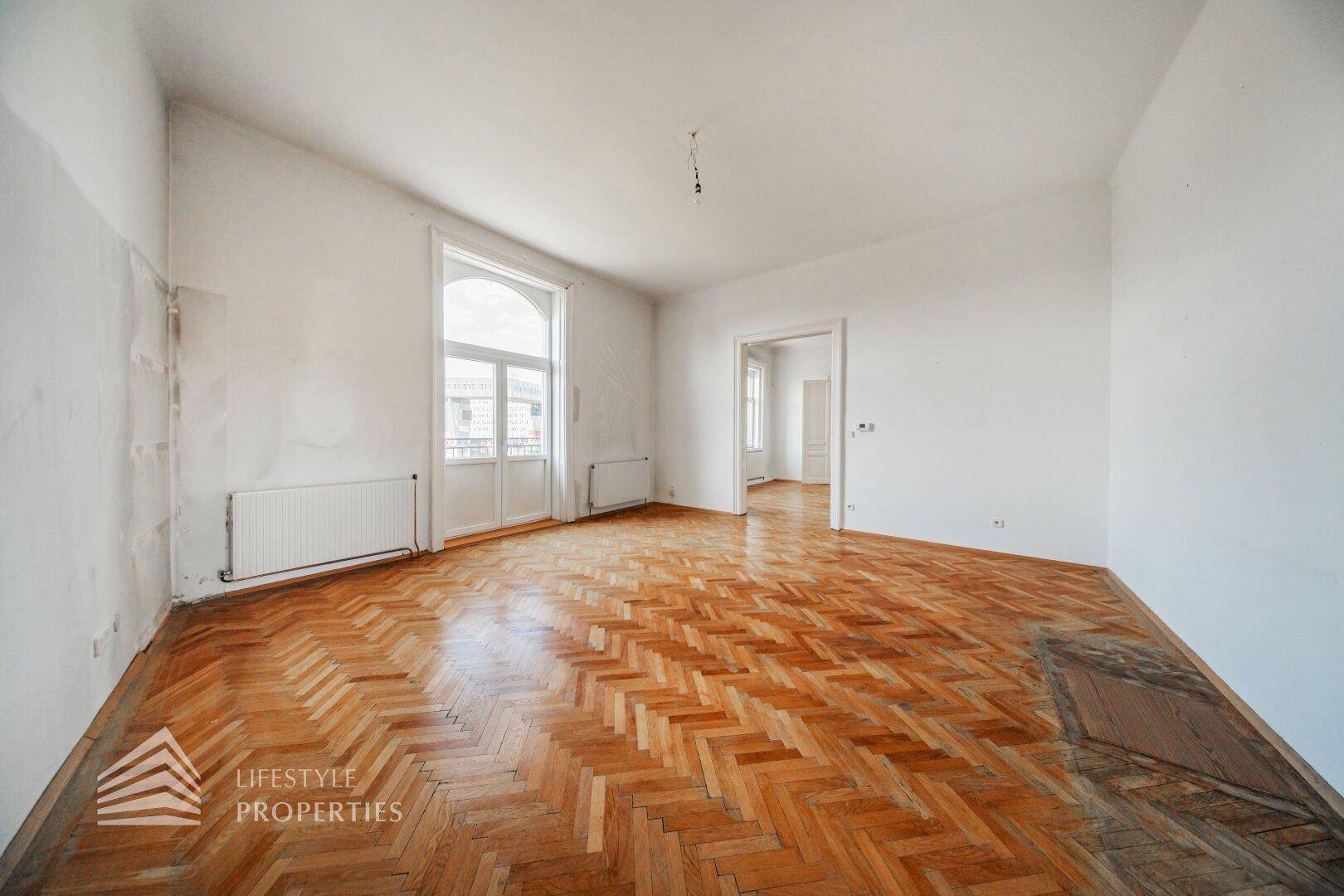 Geräumiges Wohnzimmer mit Fischgrätparkett und einem großen Fenster mit französischem Balkon.
