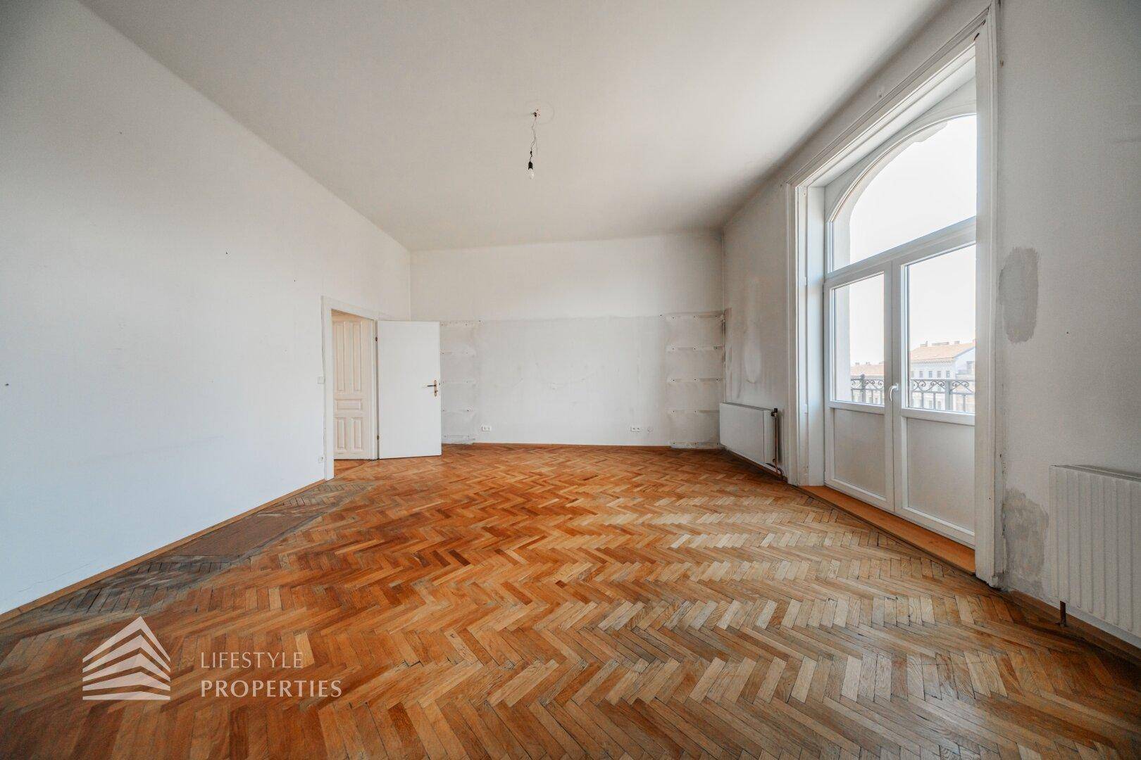 Heller Wohnraum mit Fischgrätparkett und einem hohen Bogenfenster, das viel Licht hereinlässt.