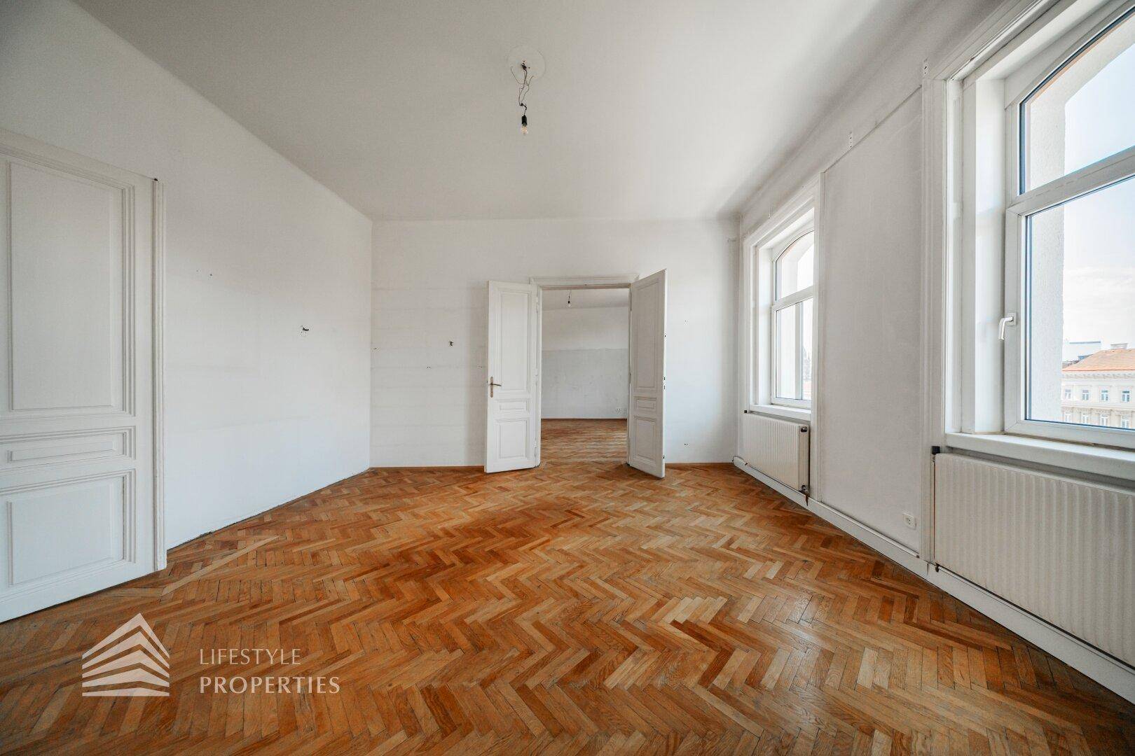 Helles Zimmer mit Fischgrätparkett und zwei Fenstern, bereit für individuelle Gestaltung.
