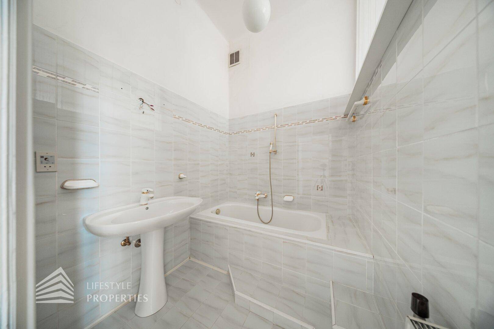 Gefliestes Badezimmer mit Badewanne und Waschbecken, in hellem, neutralem Design.