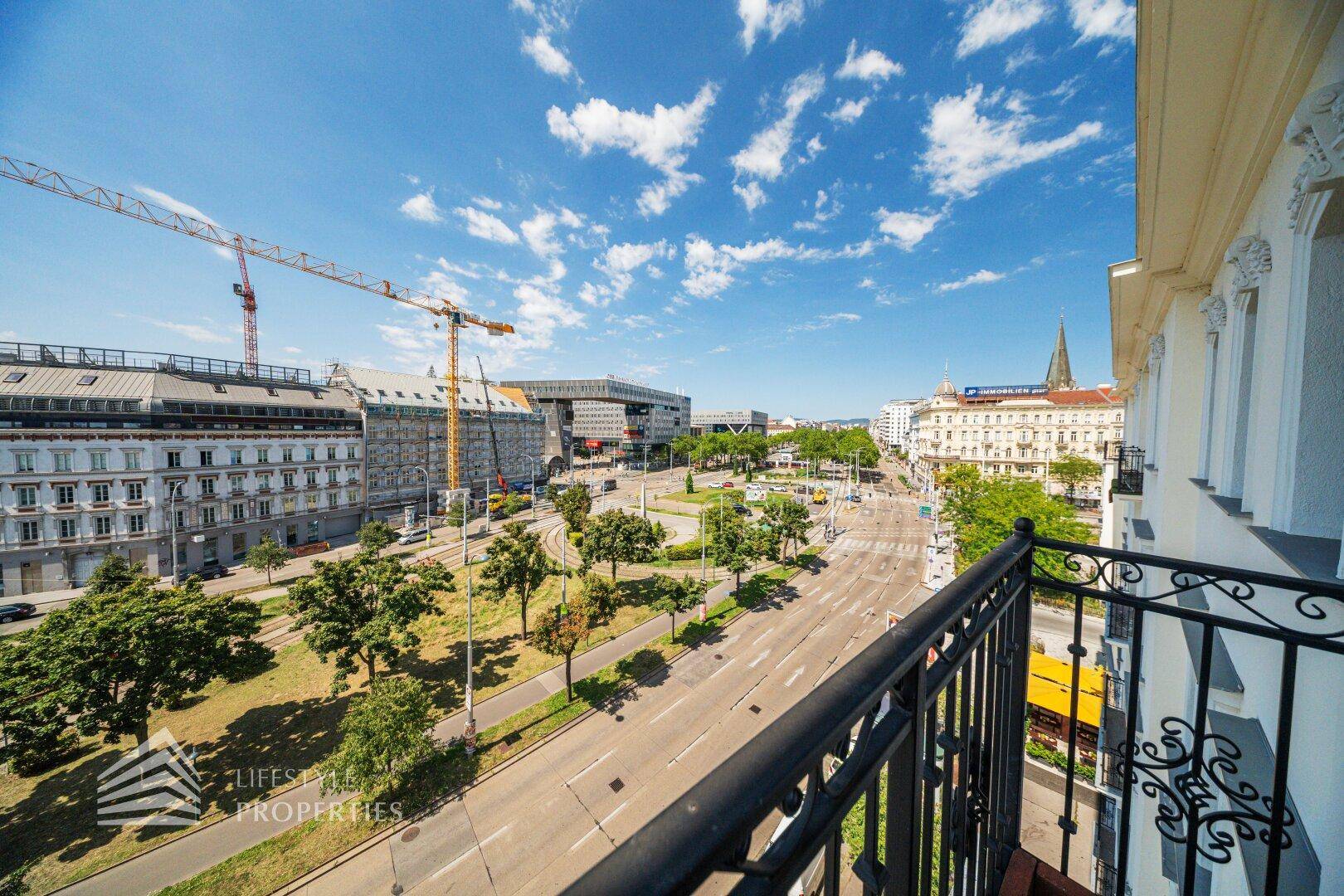 Weiter Blick vom Balkon über eine belebte Straße und die Dächer der Stadt.