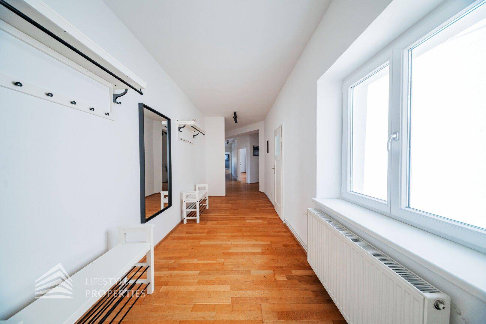 Heller Eingangsbereich mit Holzboden, Garderobe und einem großen Spiegel, der den Raum erweitert.