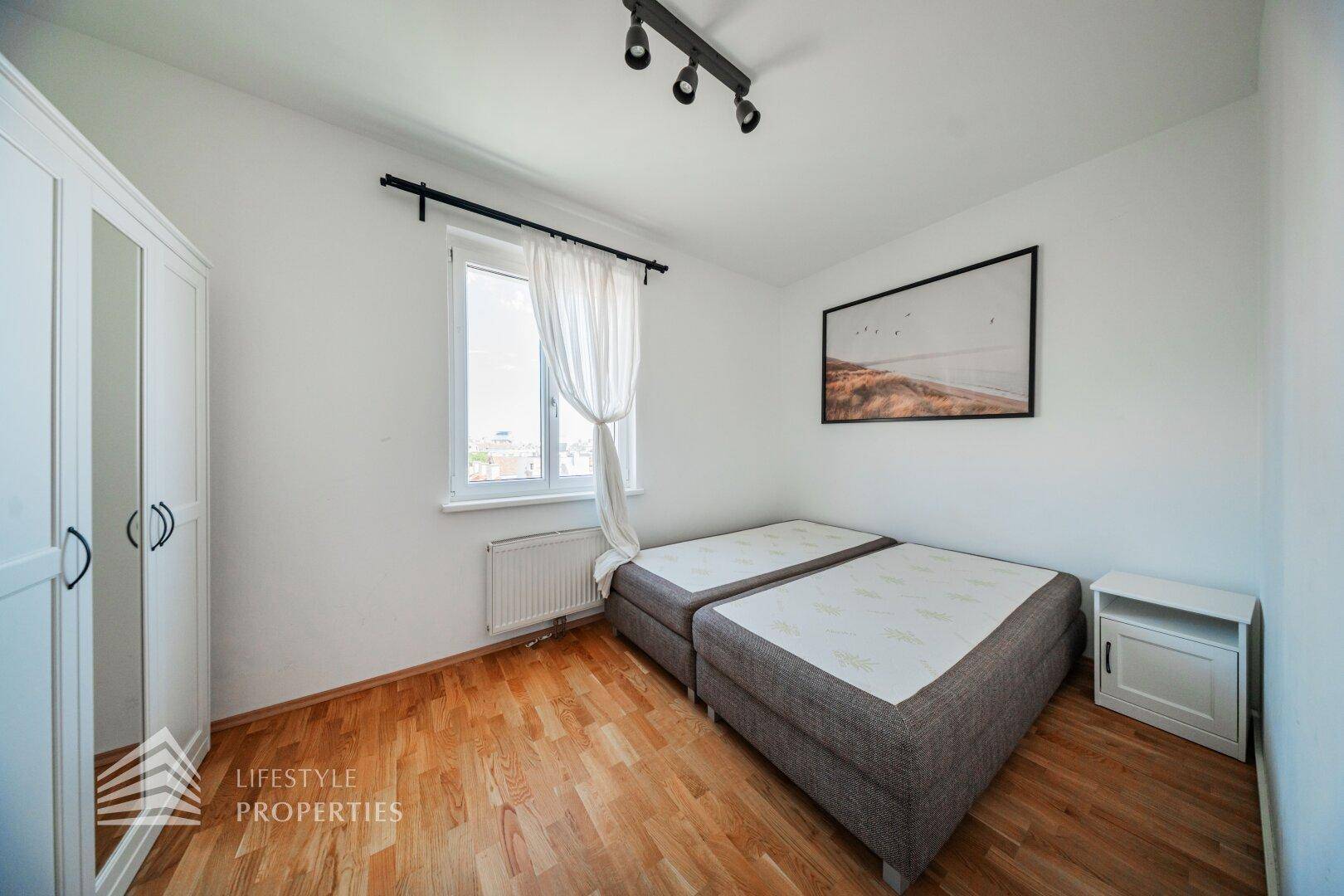 Schlafzimmer mit Holzboden, einem Fenster und einem weißen Kleiderschrank mit Spiegeltür.