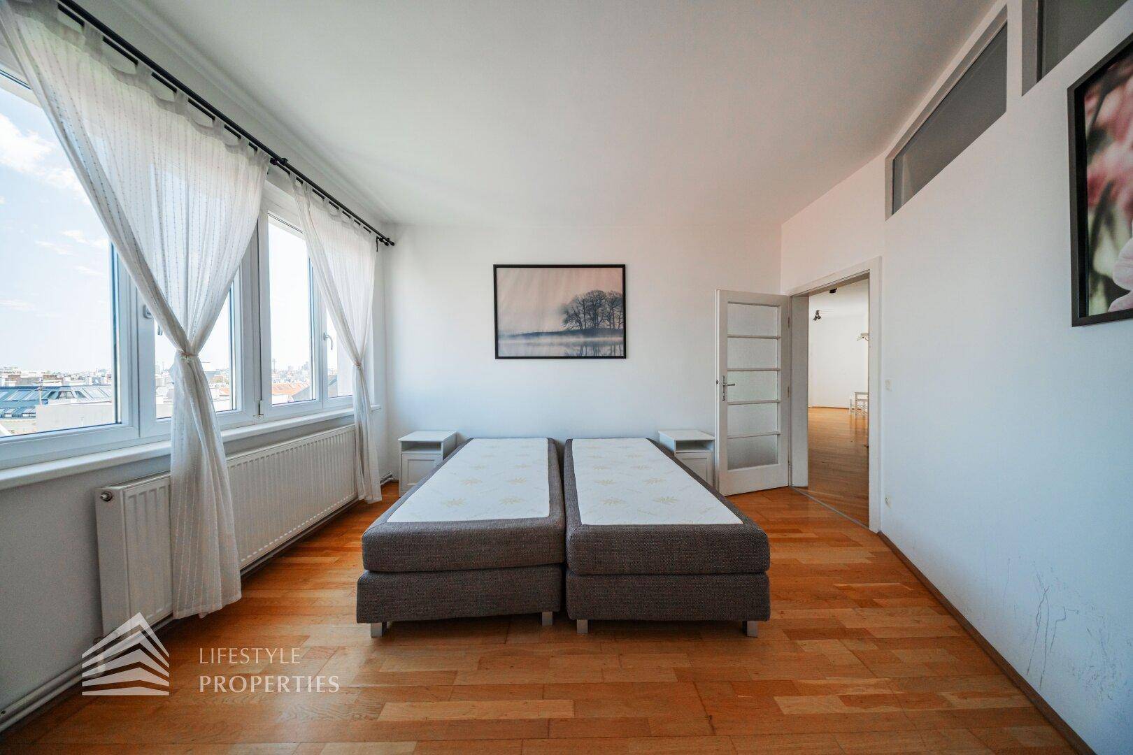 Geräumiges Schlafzimmer mit Holzboden, zwei Betten und Zugang zu einem weiteren Raum.