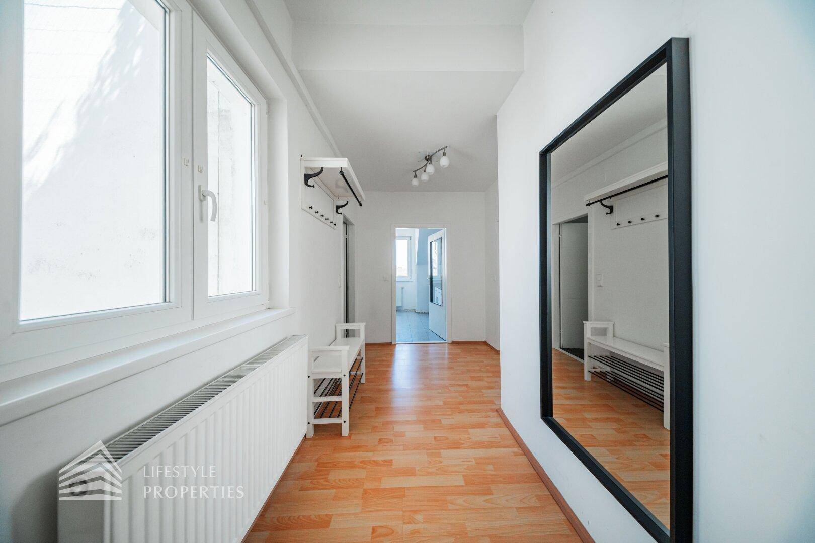 Heller Flur mit Holzfußboden, großem Spiegel und Fenster, das viel Licht hereinlässt.
