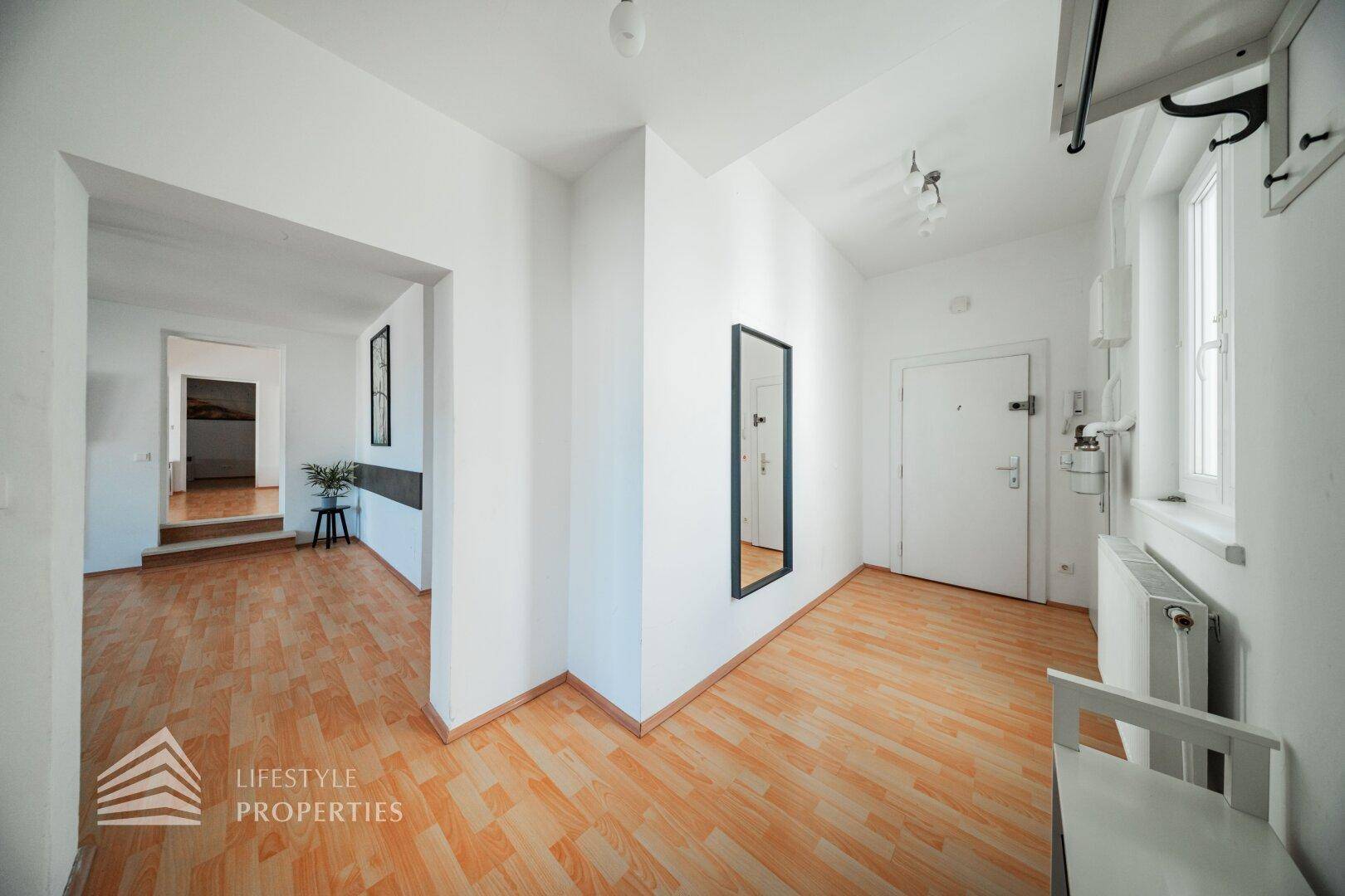 Eingangsbereich mit Holzfußboden, Spiegel und Zugang zu verschiedenen Räumen der Wohnung.