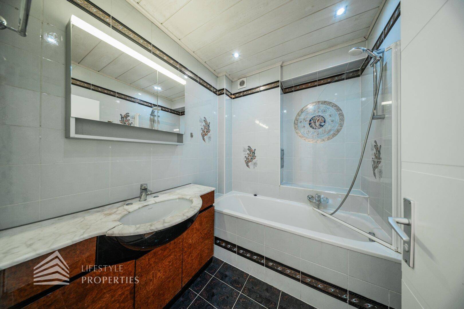 Badezimmer mit Badewanne, Marmorwaschtisch und Fliesen in hellem Blau und Schwarz.