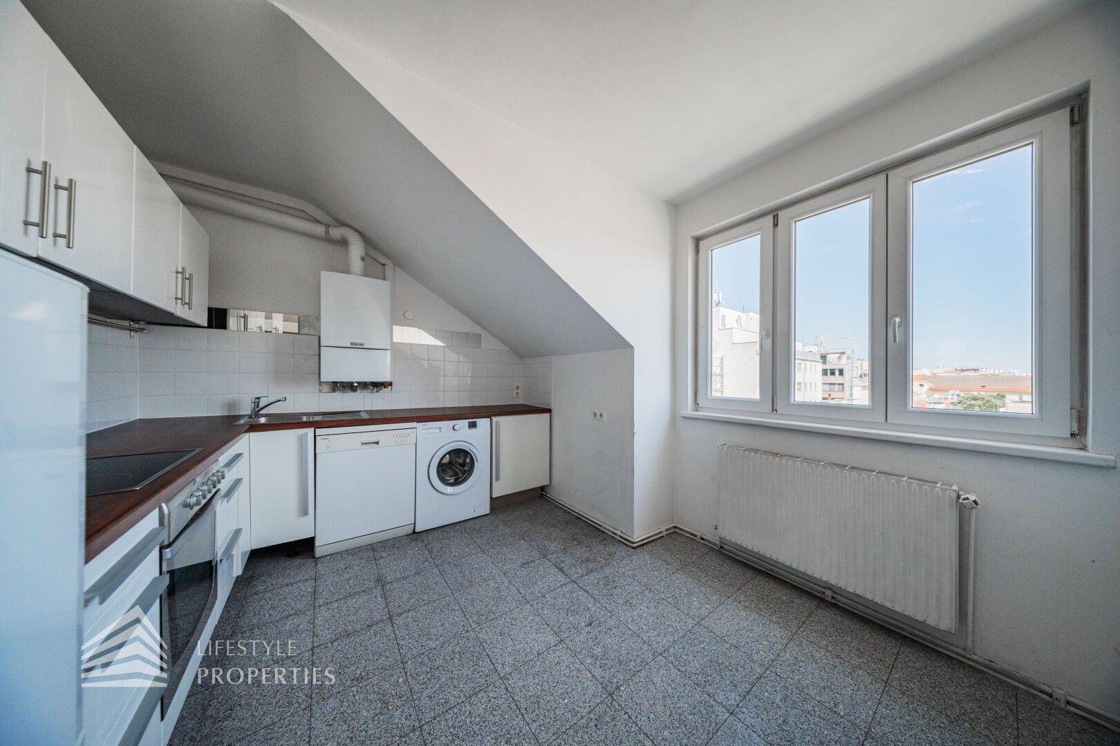 Küche im Dachgeschoss mit Einbauschränken, Waschmaschine und großem Fenster.