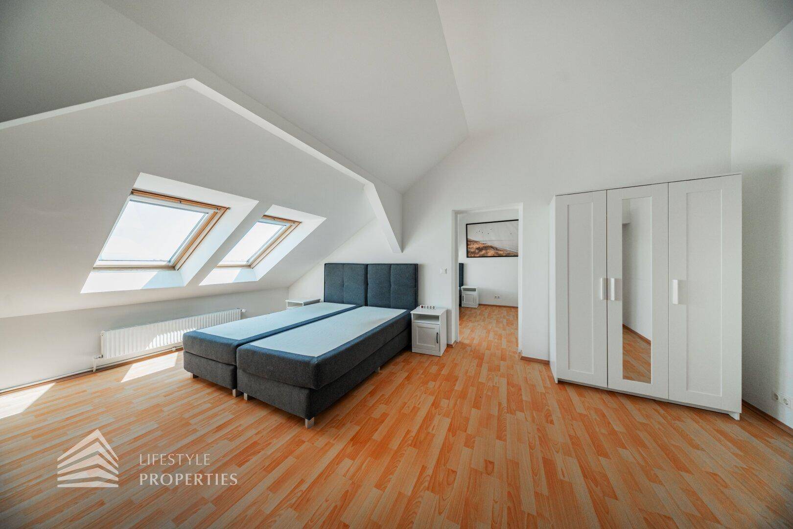 Helles Schlafzimmer im Dachgeschoss mit zwei Betten, Kleiderschrank und Dachfenstern.