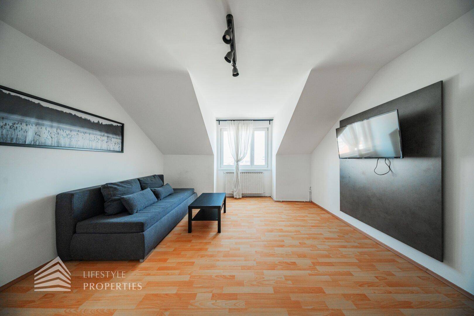 Gemütliches Wohnzimmer im Dachgeschoss mit Sofa, Fernseher und Holzfußboden.