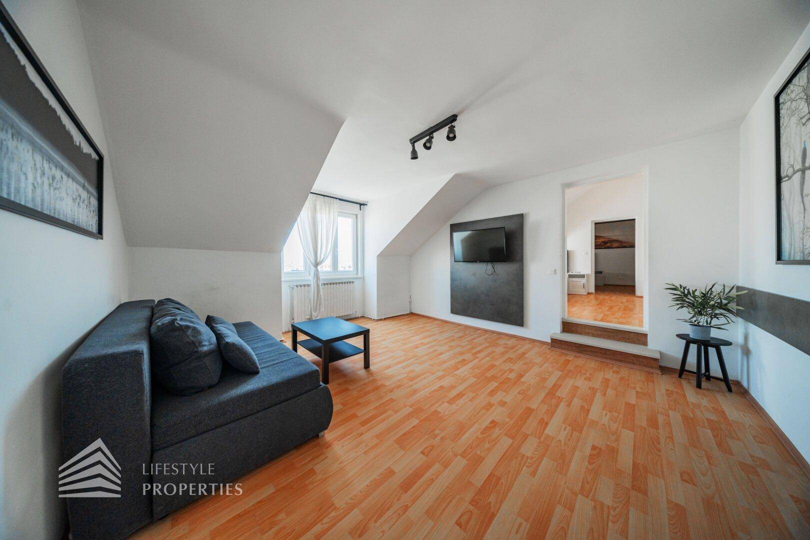 Wohnzimmer mit Sofa, Fernseher und Zugang zu einem weiteren Raum, ausgestattet mit Holzfußboden.