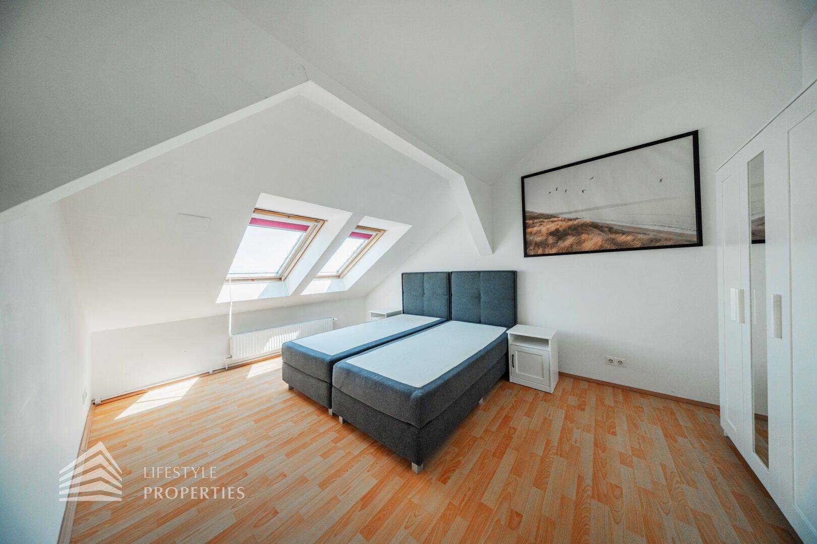 Schlafzimmer im Dachgeschoss mit zwei Betten, Kleiderschrank und viel natürlichem Licht durch Dachfenster.