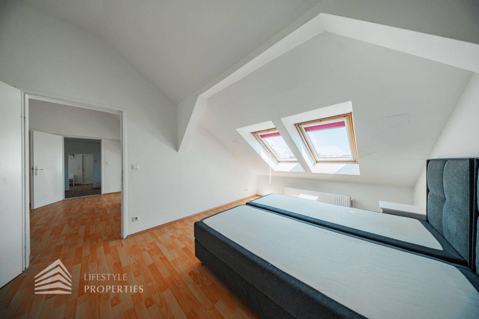 Schlafzimmer im Dachgeschoss mit zwei Betten, Dachfenstern und Zugang zu einem weiteren Raum.