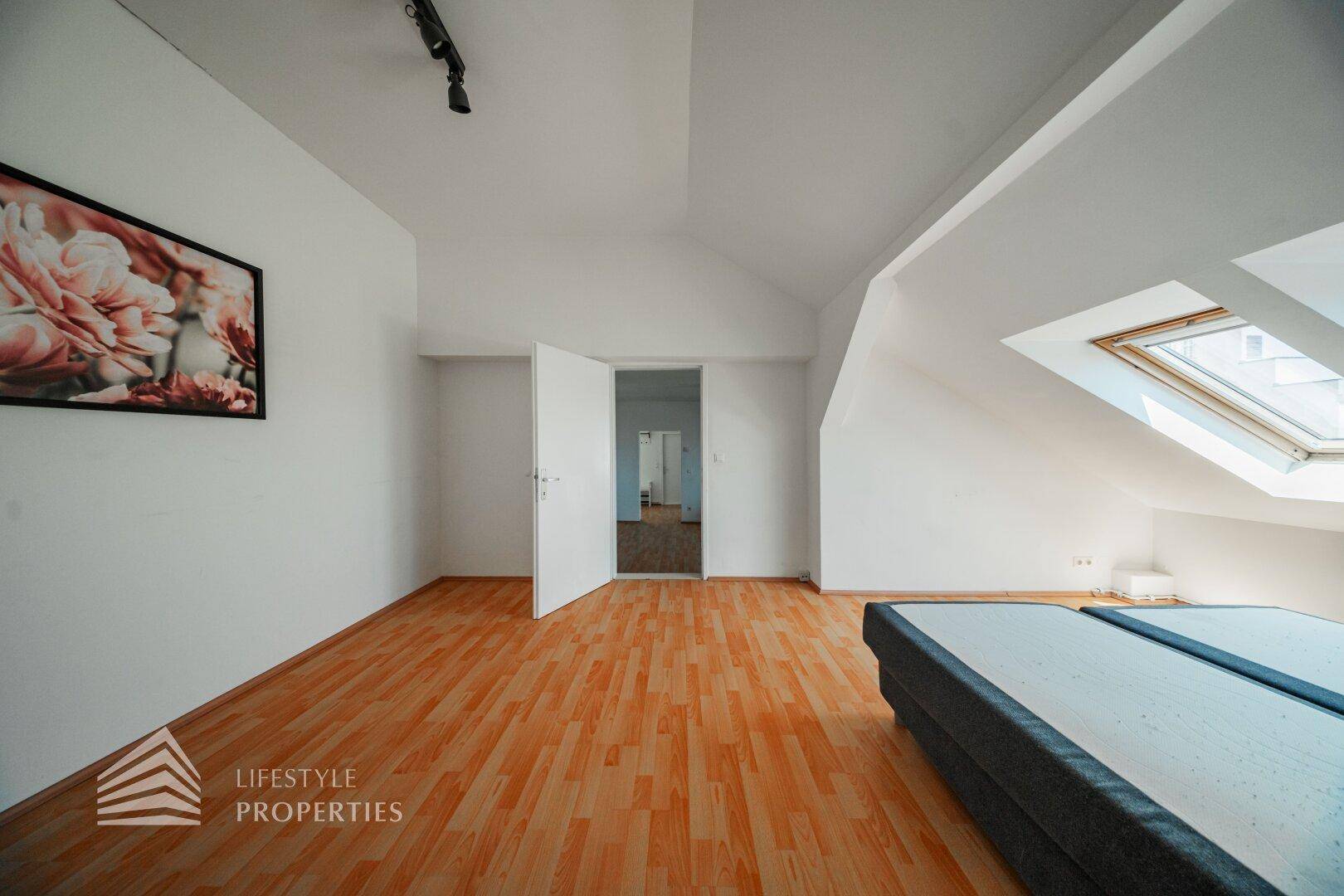 Geräumiges Schlafzimmer im Dachgeschoss mit Holzfußboden, Dachfenster und Zugang zu anderen Räumen.