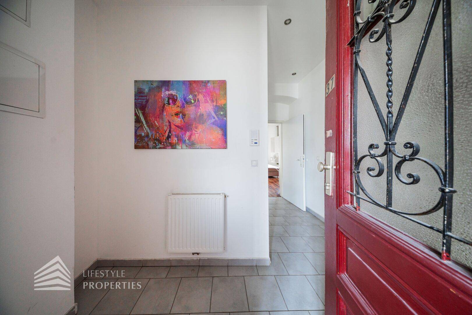 Eingangsbereich mit roter Tür, Fliesenboden und farbenfrohem Kunstwerk an der Wand.